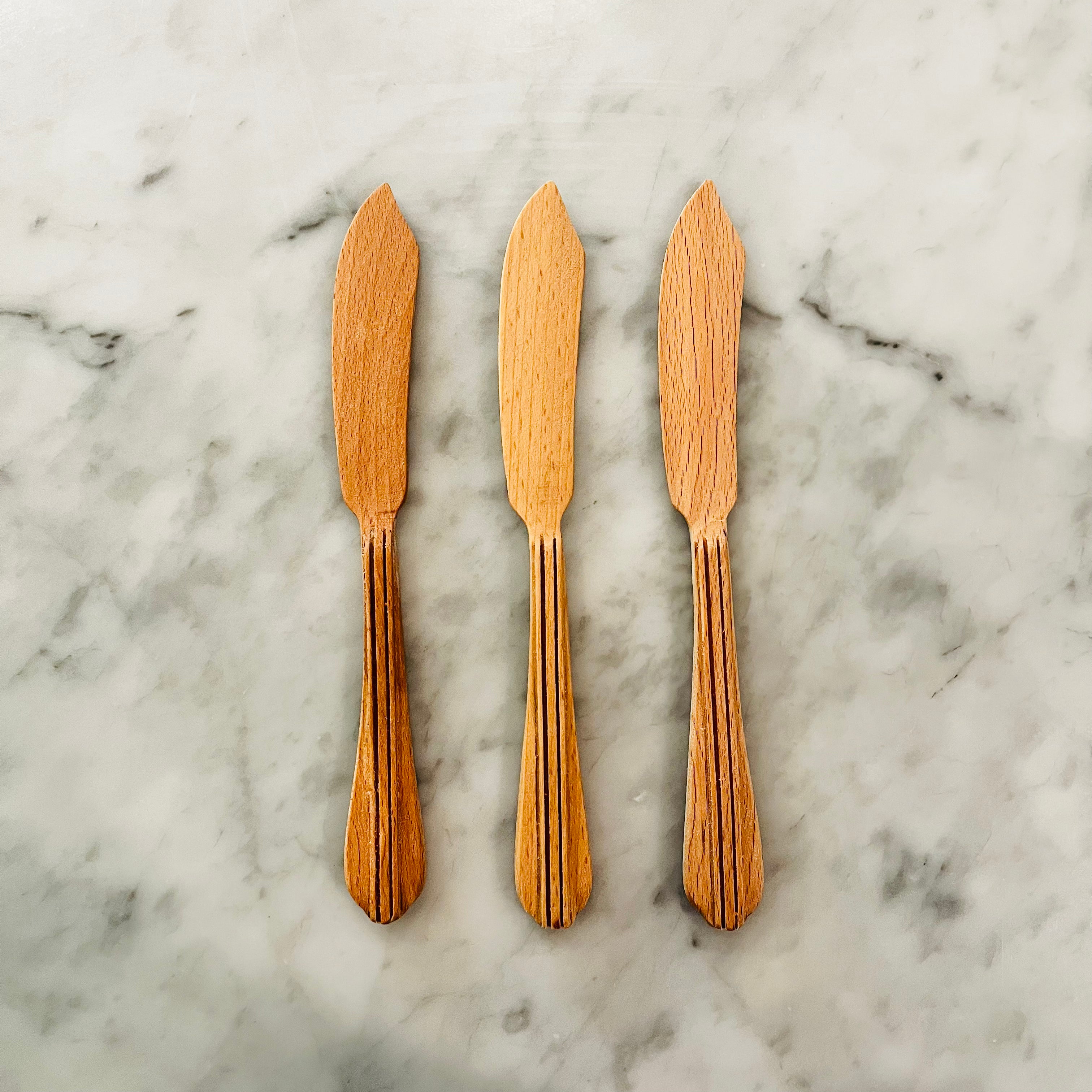 Three wooden butter spreaders with pointed tips arranged vertically on marble surface