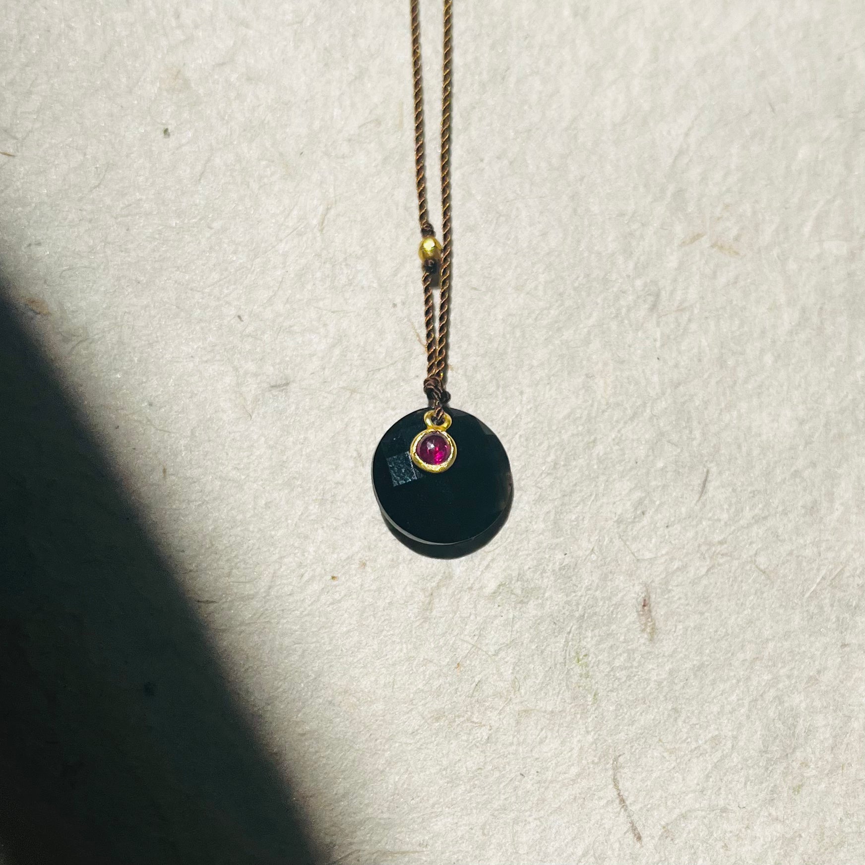 Obsidian and ruby necklace with black circular pendant on bronze chain against white background