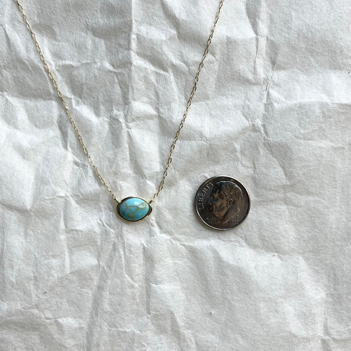 Cabochon turquoise pendant necklace on white fabric next to dime for size comparison