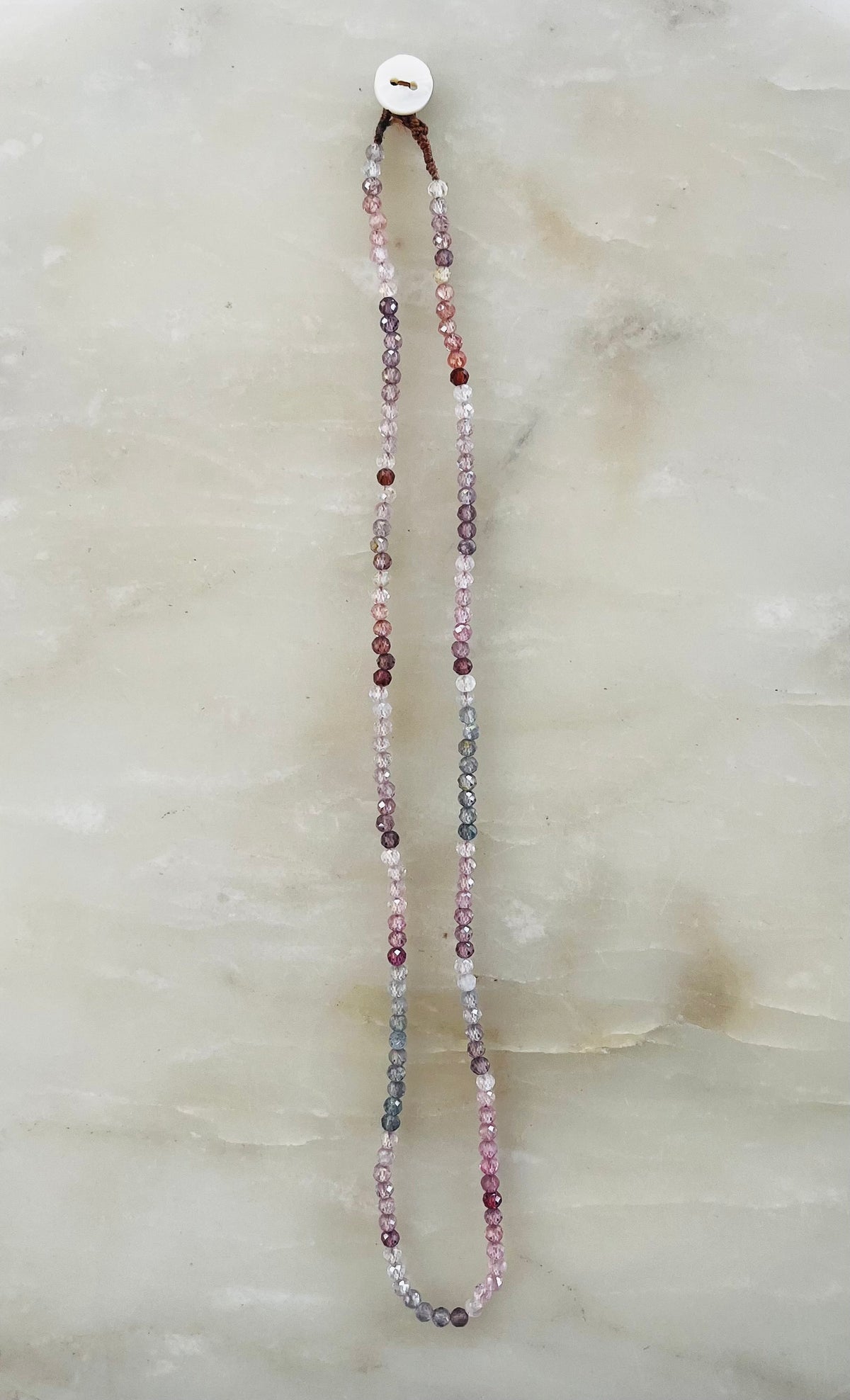 Long beaded necklace with pink, gray, and burgundy sapphire stones hanging on white button