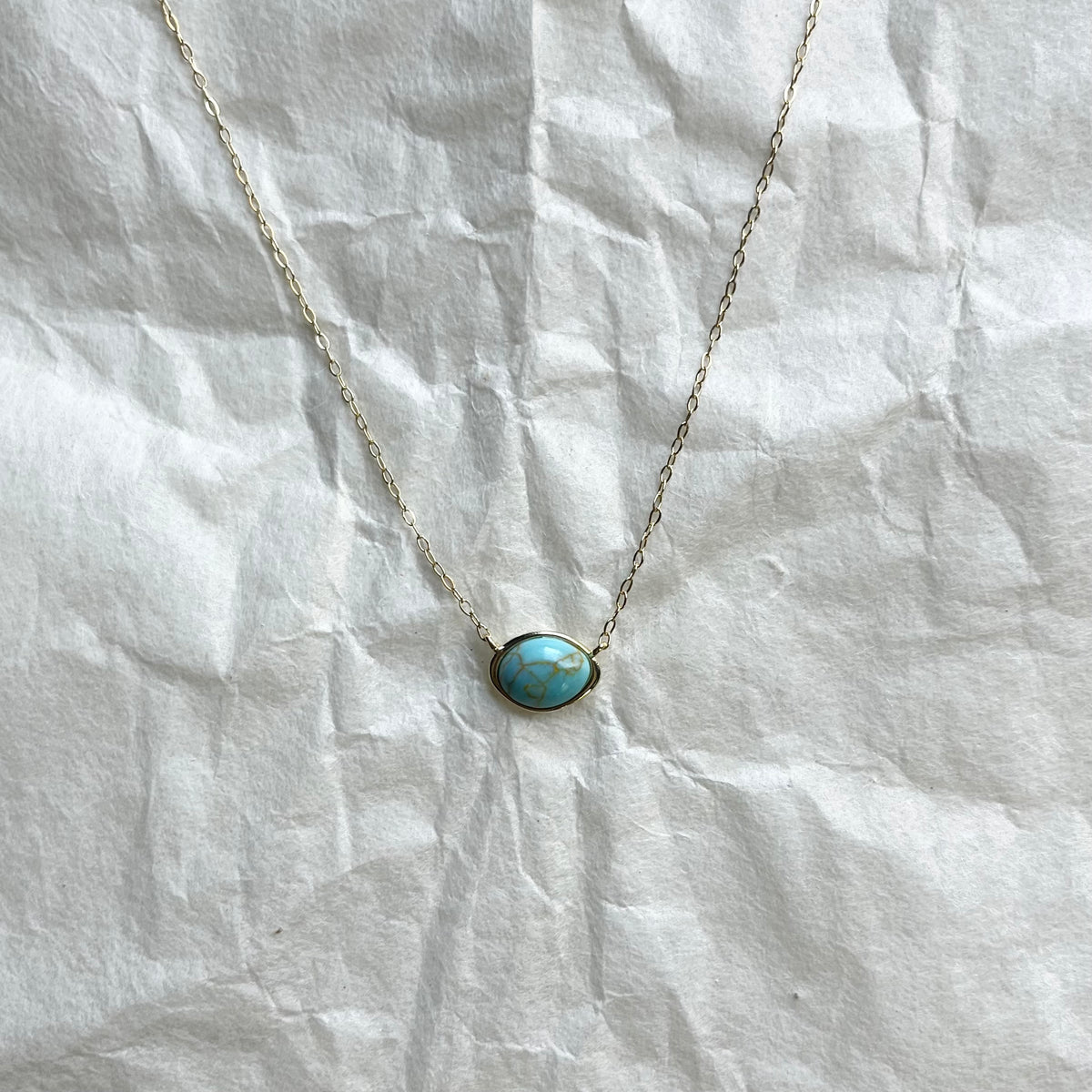 Delicate gold chain necklace with small oval turquoise cabochon pendant on white fabric
