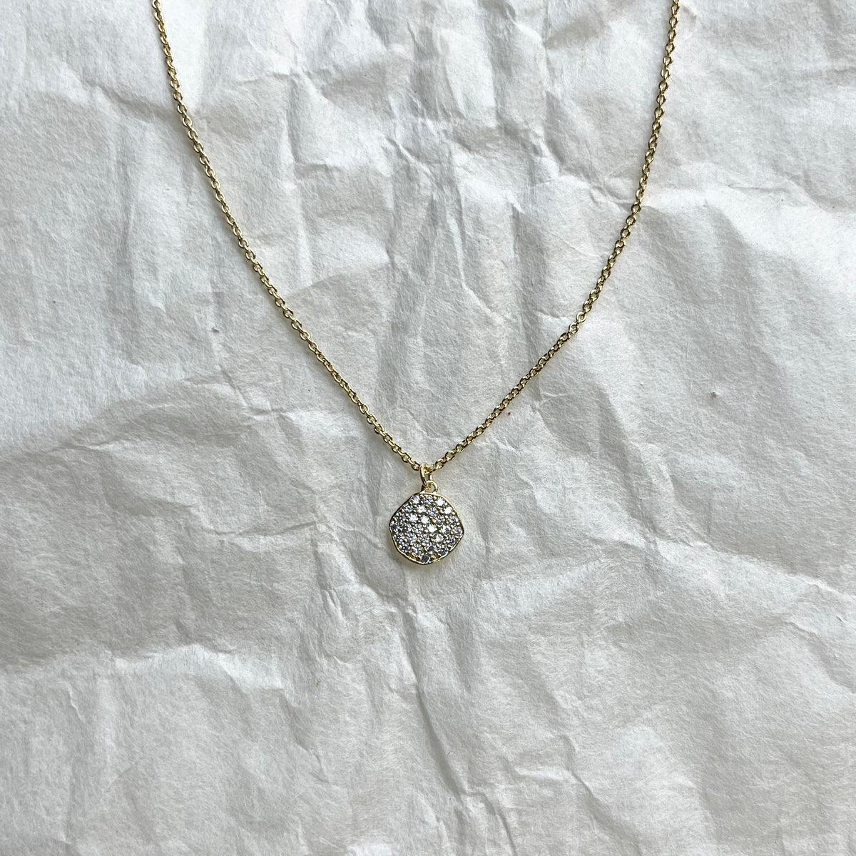 Gold chain necklace with small round cubic zirconia disc pendant on white fabric