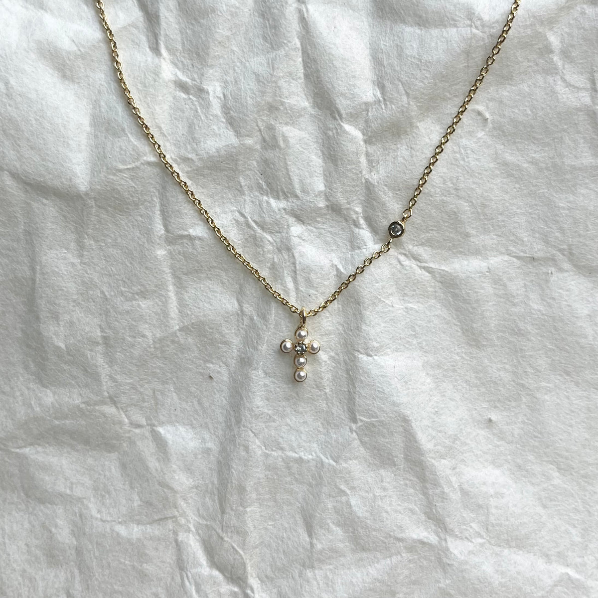 Gold chain necklace with small pearl cross pendant and single accent stone