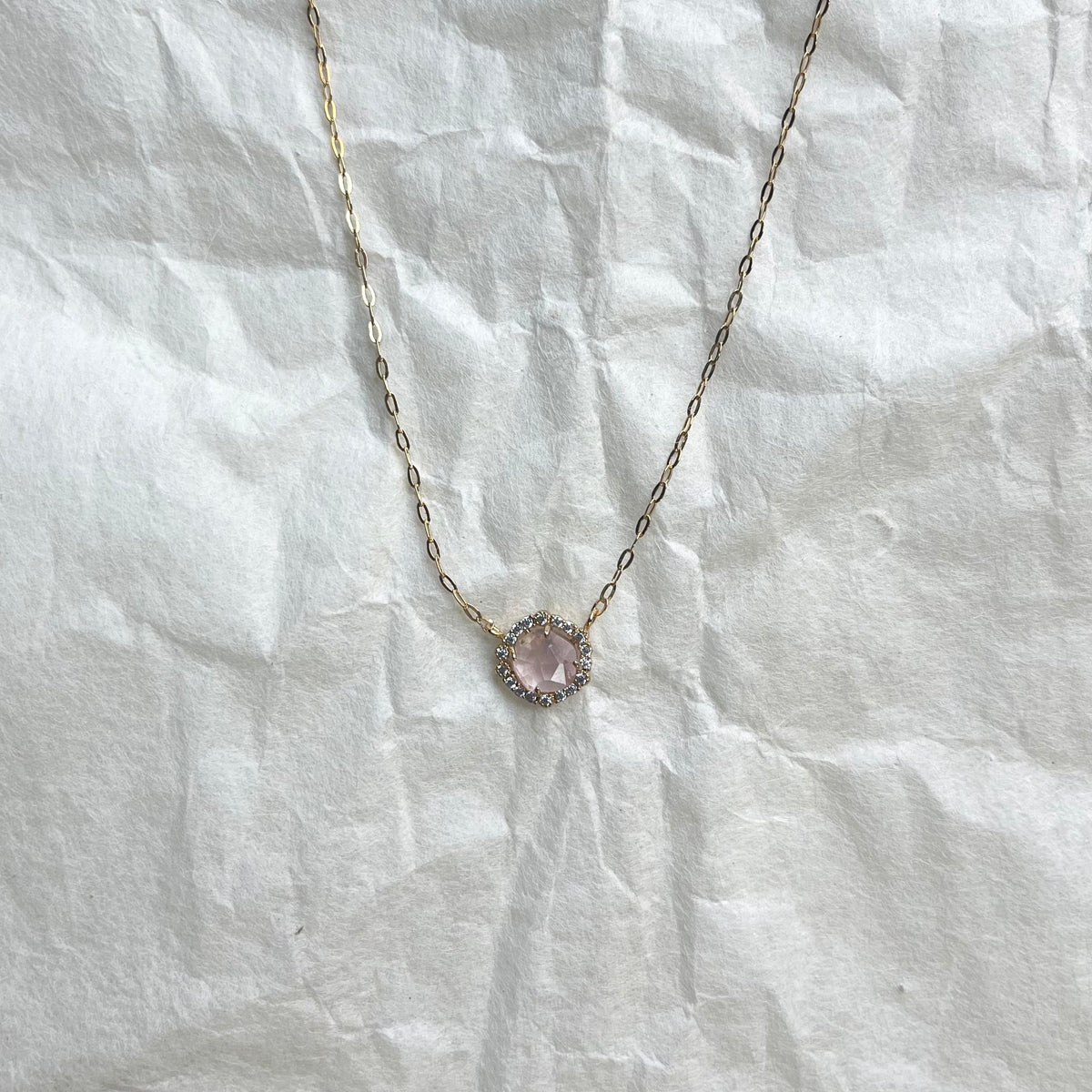 Gold chain necklace with pink faceted glass pendant surrounded by small clear stones