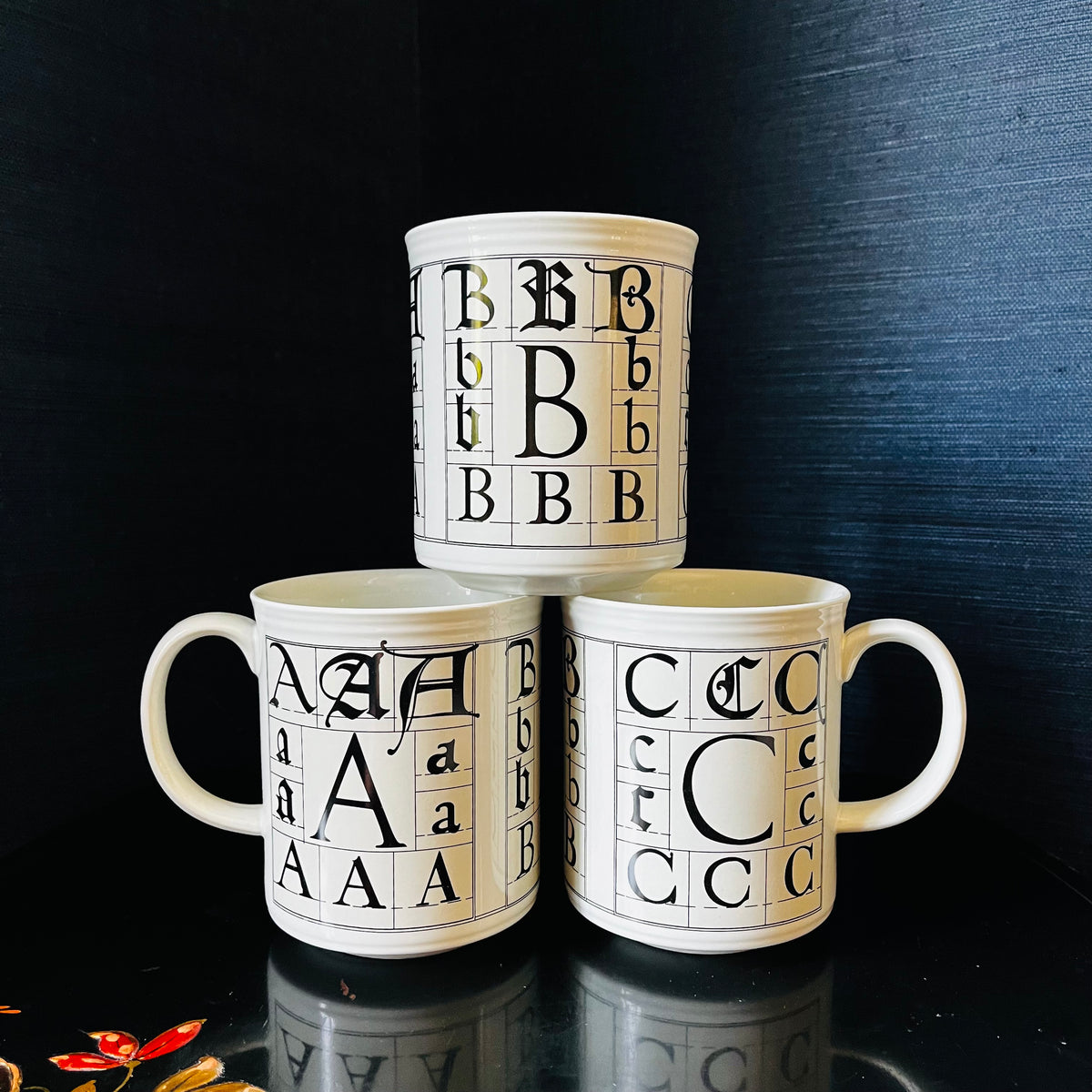 Three stacked calligraphy alphabet mugs displaying different letters A, B, and C in various fonts