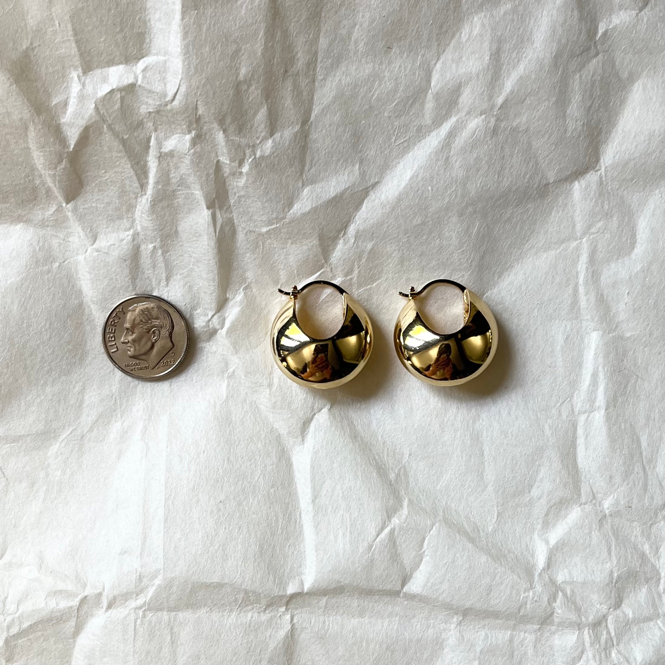 Gold huggie hoop earrings next to dime for size comparison on white fabric