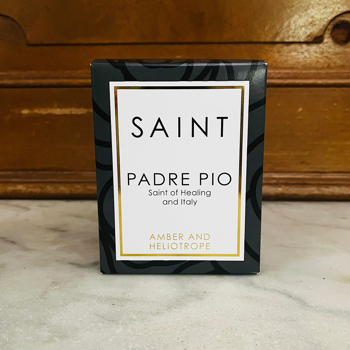 Saint Padre Pio candle box in amber and heliotrope scent on wooden surface