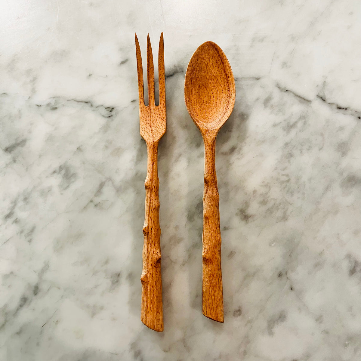 Wooden fork and spoon with natural branch-style handles on marble surface