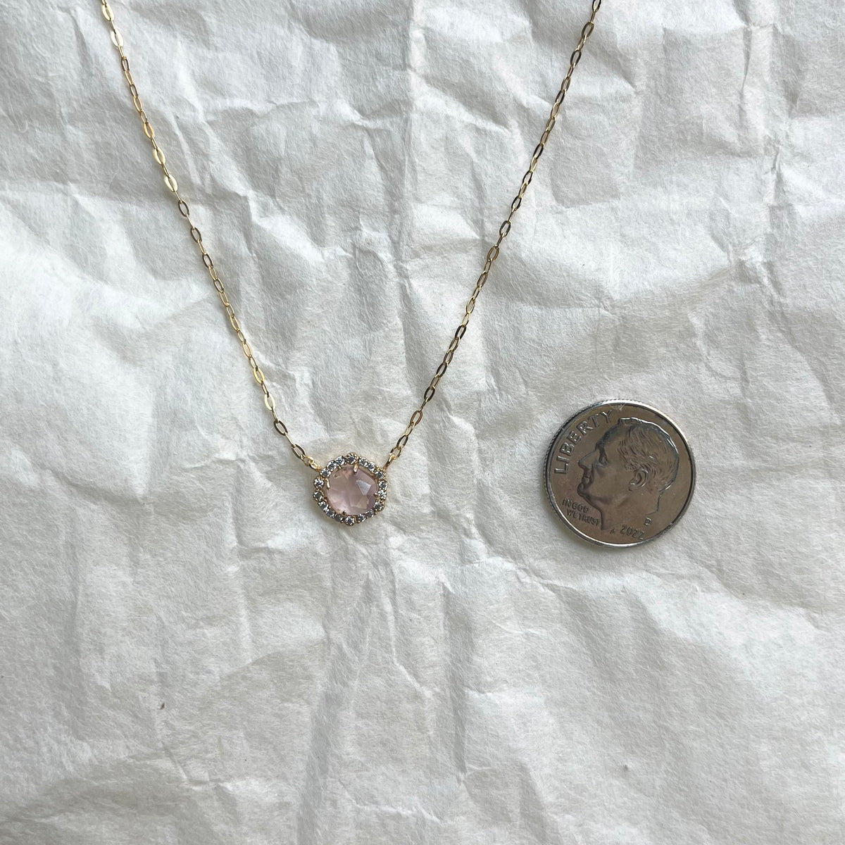 Bezel glass pendant necklace with pink stone and crystals next to dime for scale