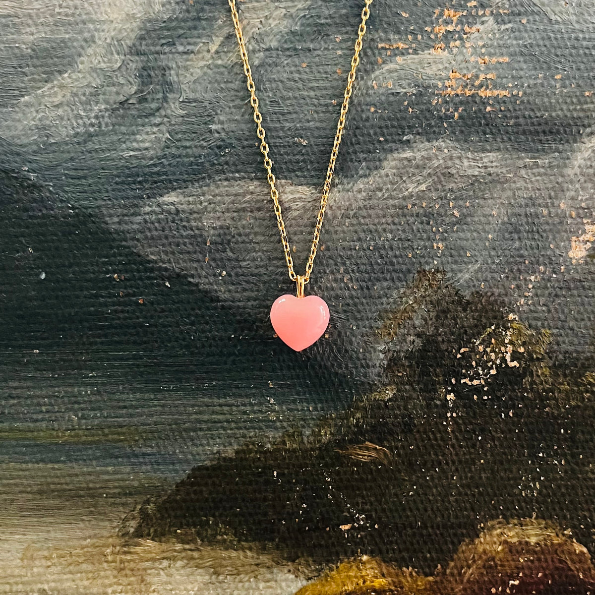Pink heart pendant on gold chain necklace displayed against textured painted canvas background
