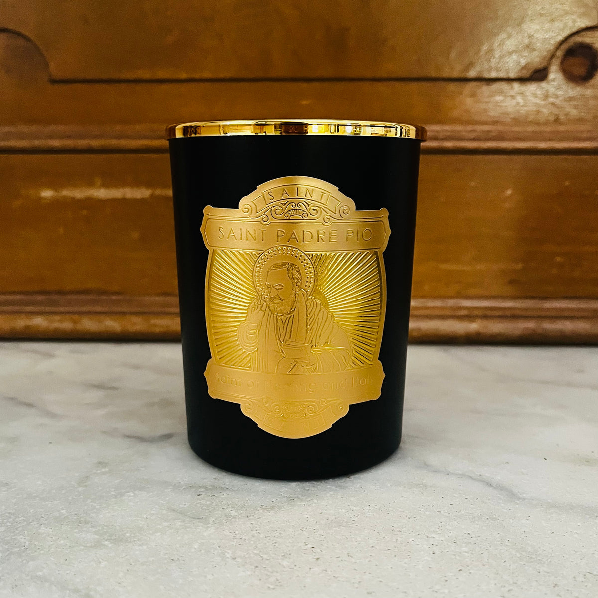 Black candle with gold medallion featuring Saint Padre Pio image and text