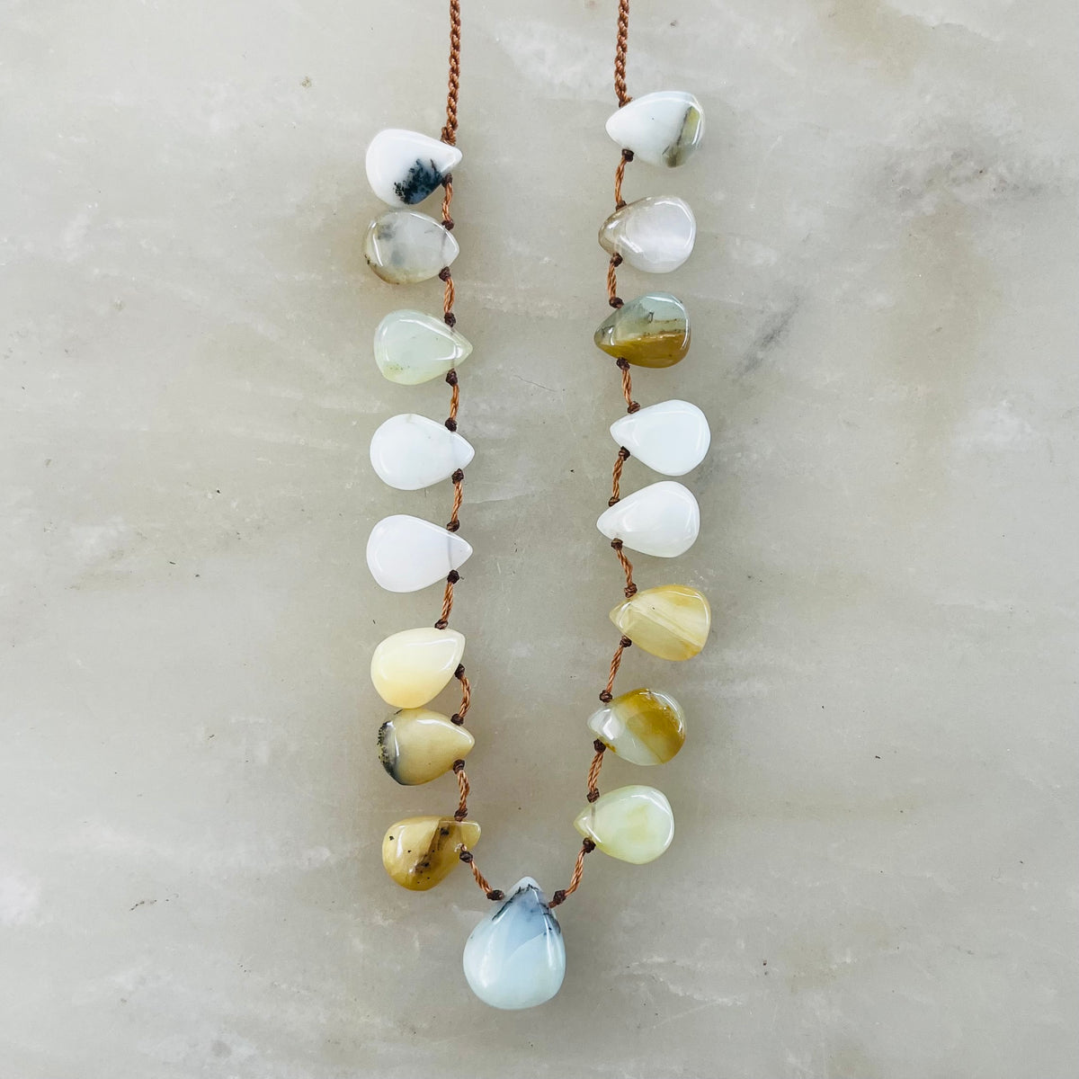 Opal necklace with teardrop-shaped stones in white, yellow, and blue tones on brown cord