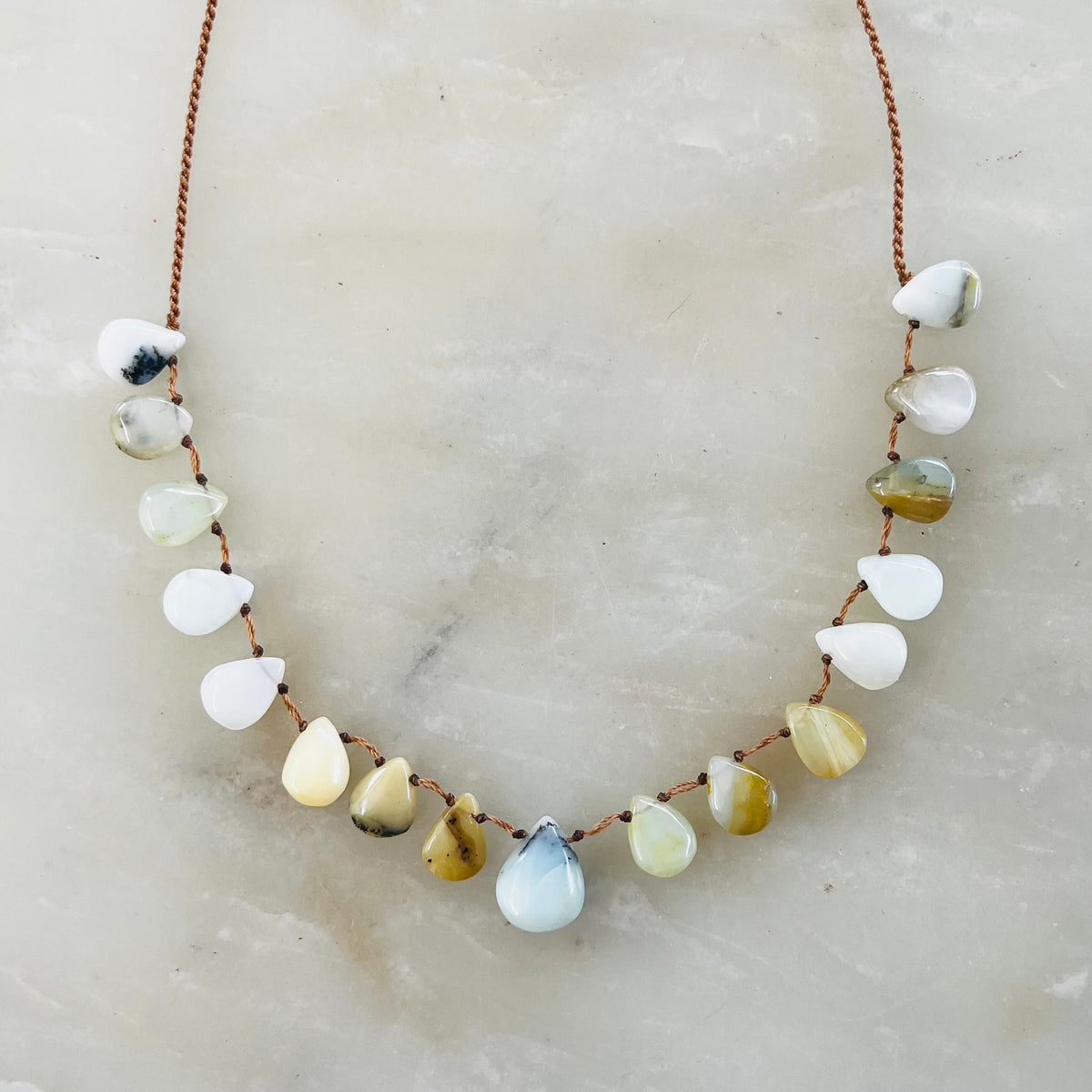 Opal necklace with teardrop-shaped stones on copper chain against white marble surface