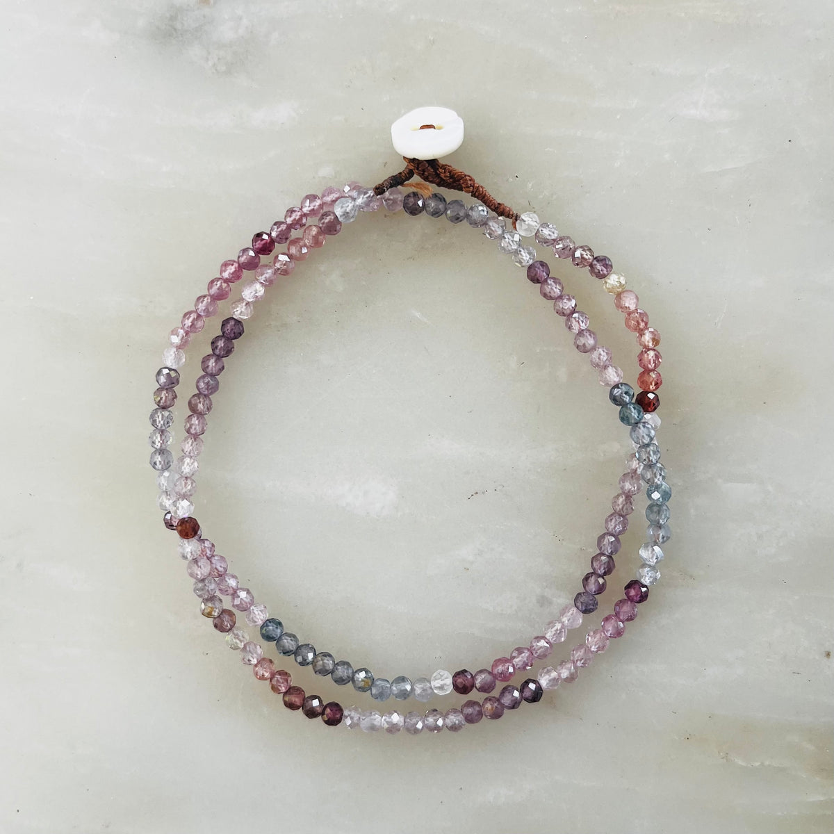 Two-strand pink sapphire beaded necklace with white button closure on neutral background