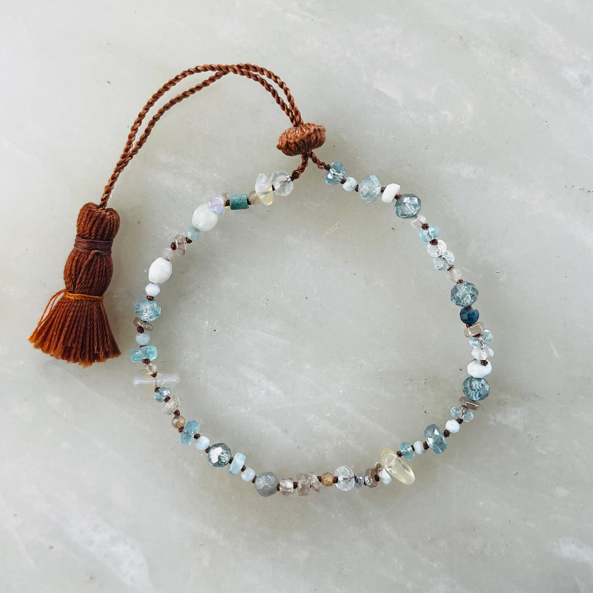 Rainbow Opal bracelet with mixed blue, white, and clear beads and brown tassel