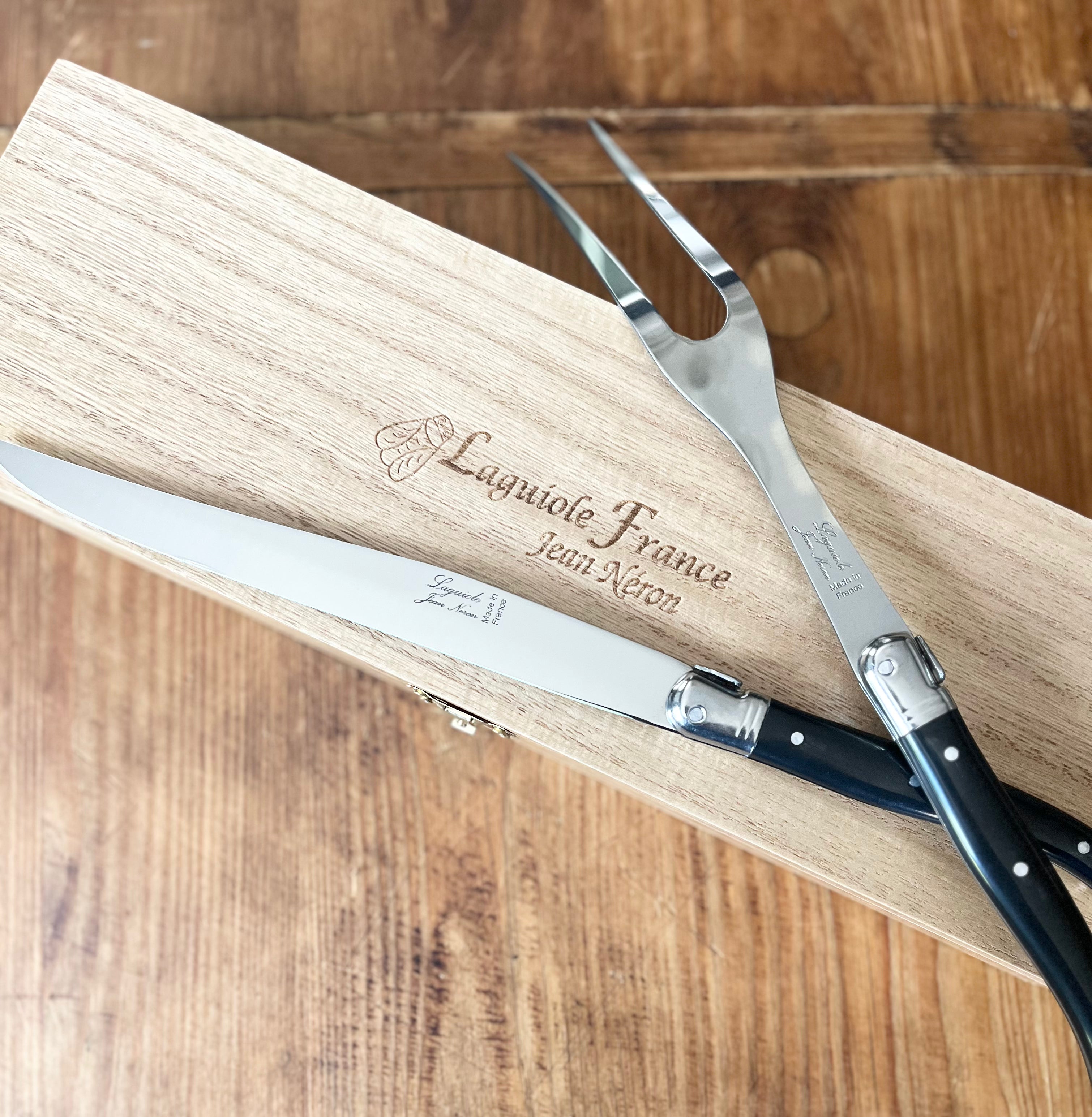 Laguiole carving knife and fork resting on wooden cutting board with engraved text