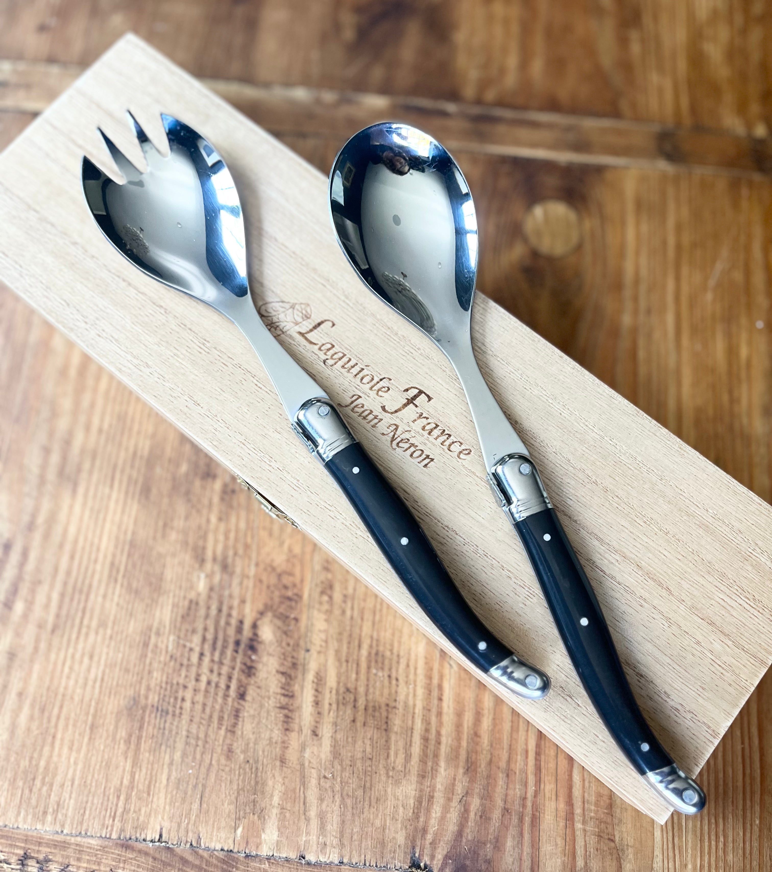 Laguiole salad serving fork and spoon with black handles on wooden presentation board