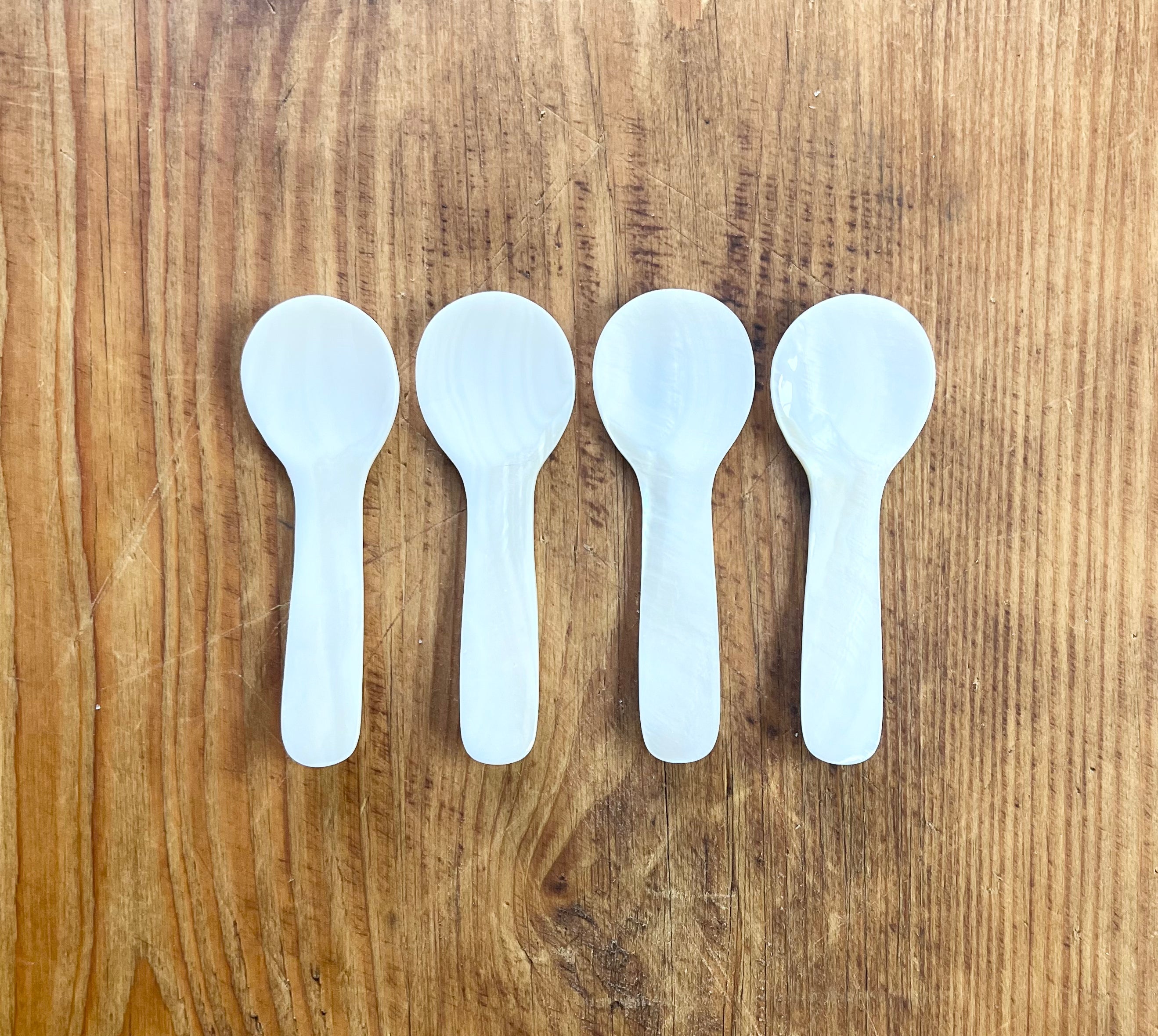 Four white mother of pearl spoons arranged in a row on wooden surface