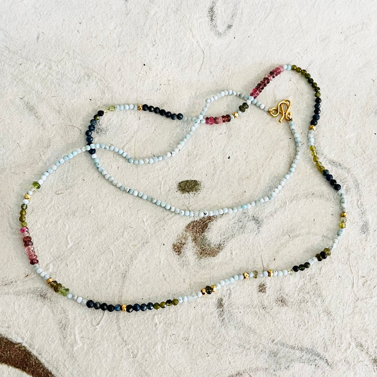 Colorful beaded necklace with white, pink, green, and black gemstone beads with gold clasp