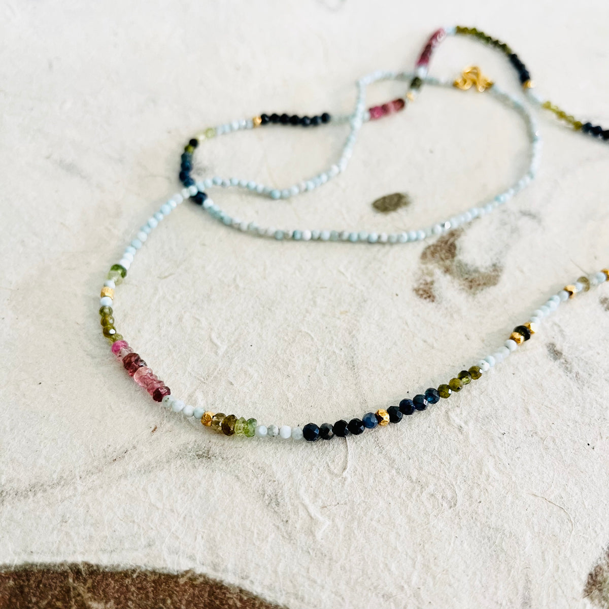 Three colorful beaded necklaces with varied gemstones arranged on white textured surface