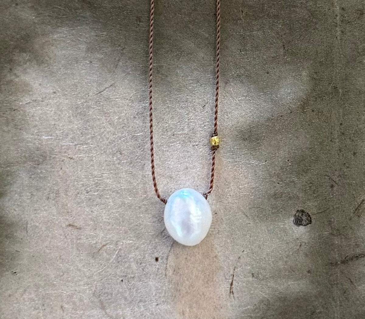 The Sister Pearls necklace with white pearl pendant and small yellow bead on brown cord