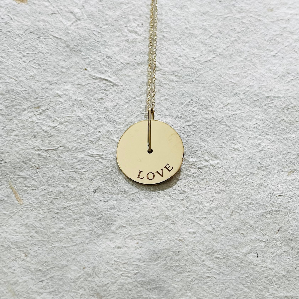 Gold circular pendant necklace engraved with the word LOVE on white textured background