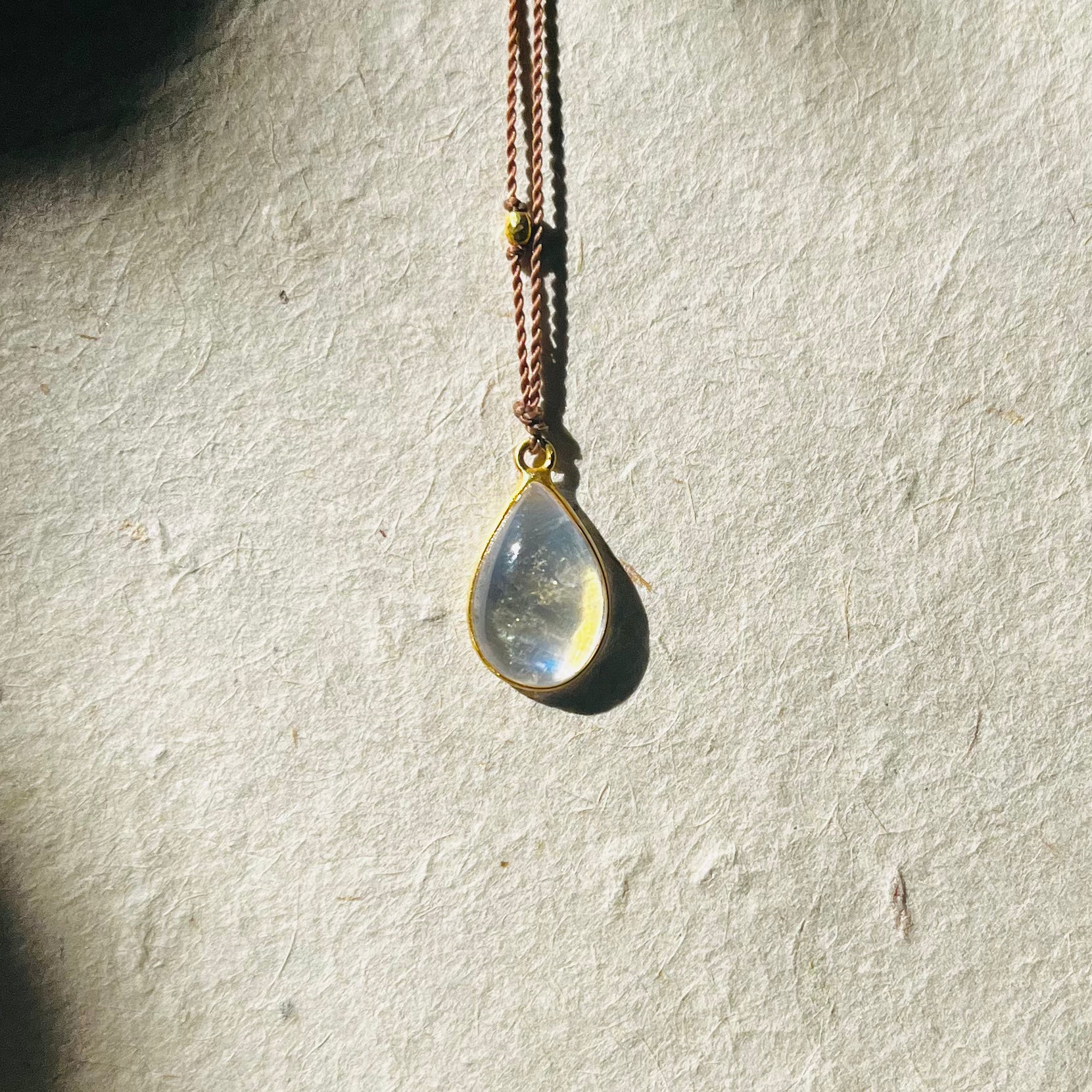 Teardrop moonstone pendant with gold bezel on copper chain against textured white background