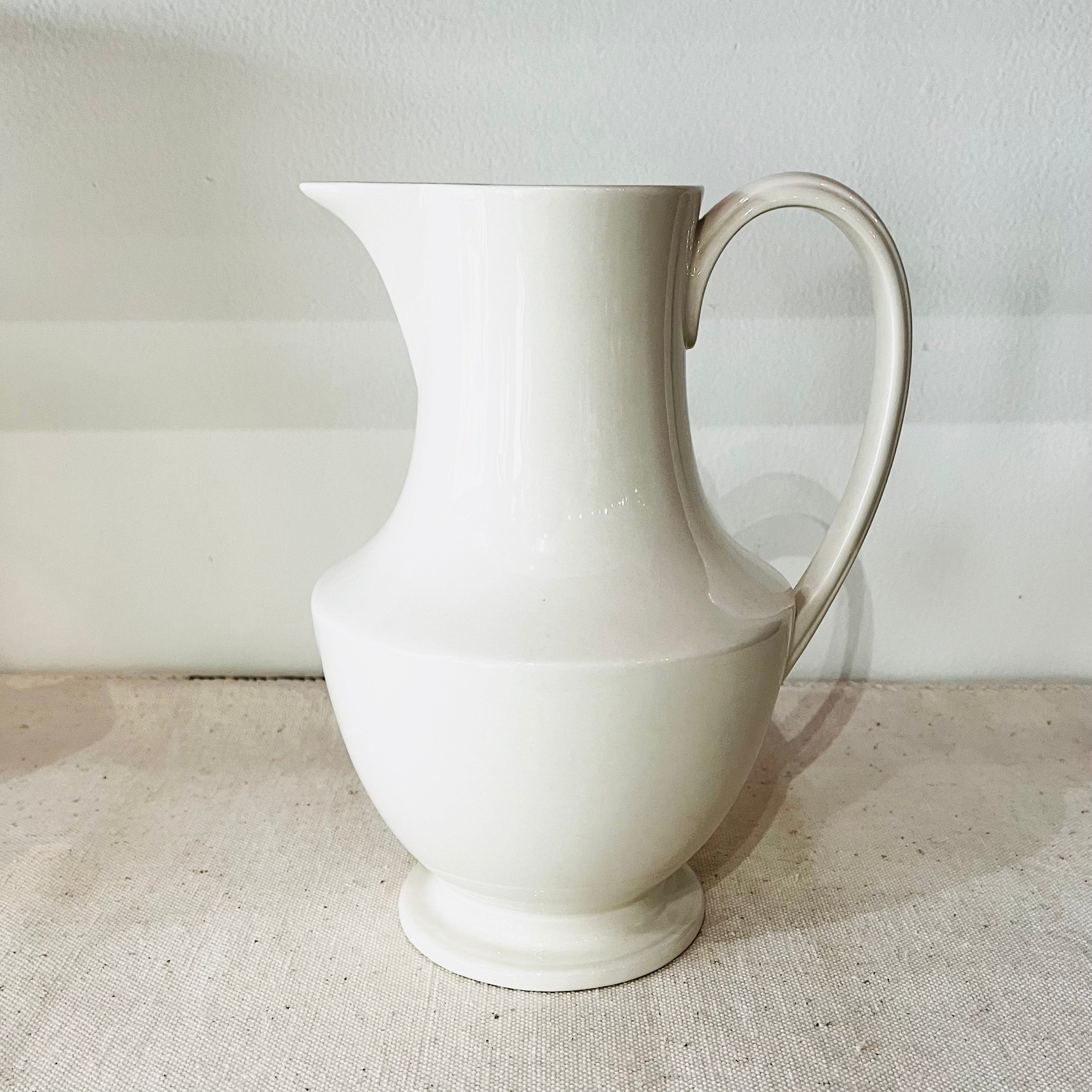 White ceramic Toulouse medium pitcher with curved handle on beige surface