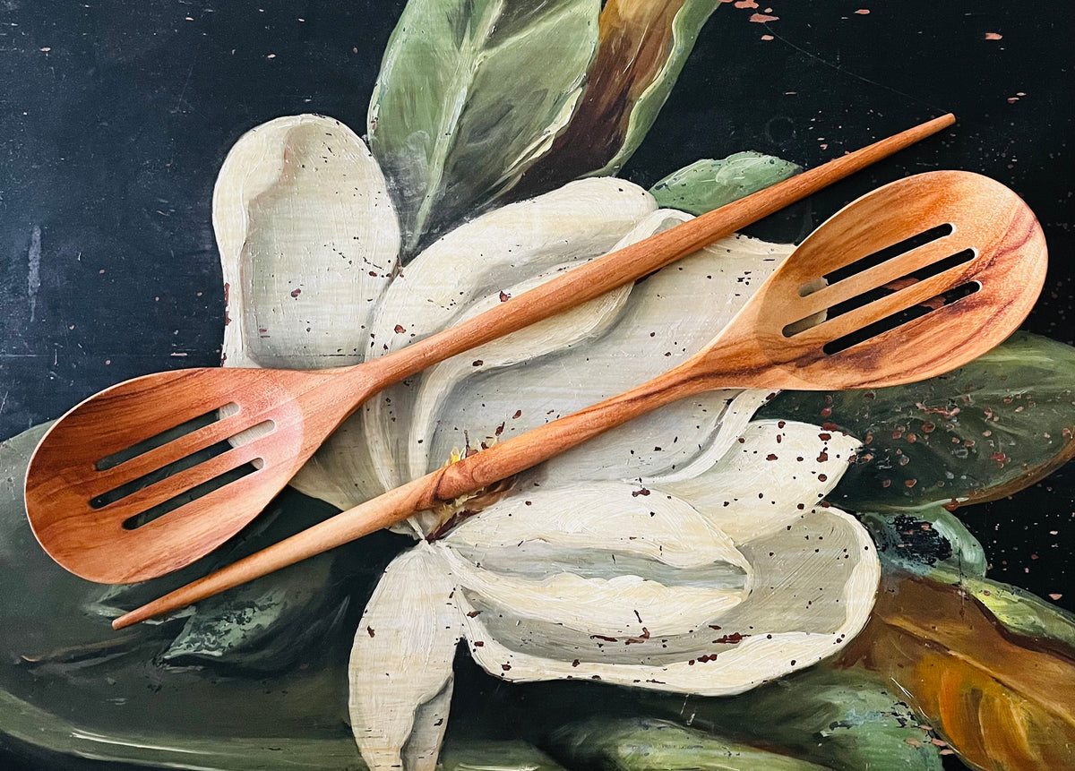 Two teak slotted spoons crossed on painted white flowers with green leaves