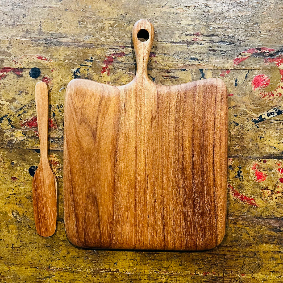 Square oak cheese board with handle and wooden spreader knife on painted wood surface
