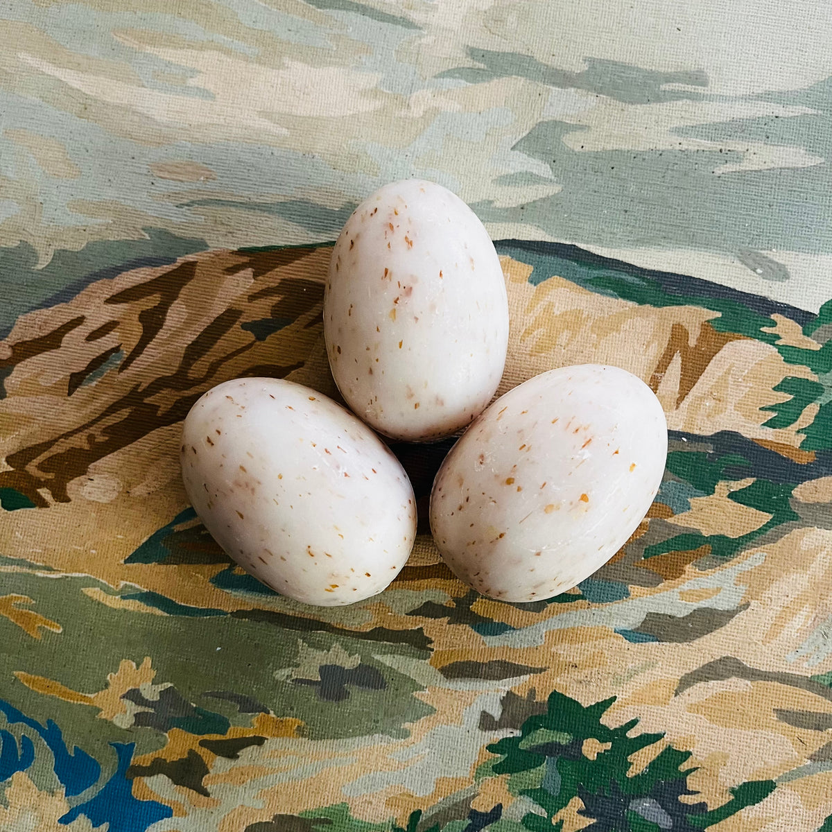 Three white speckled egg soaps stacked on a floral fabric background