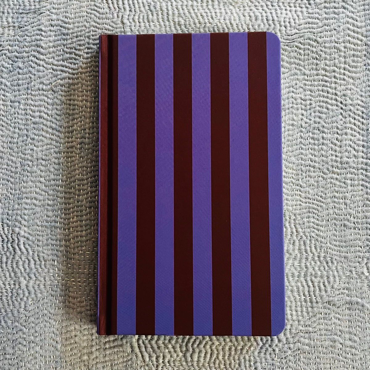Purple and nutmeg striped journal with spiral binding on textured fabric surface