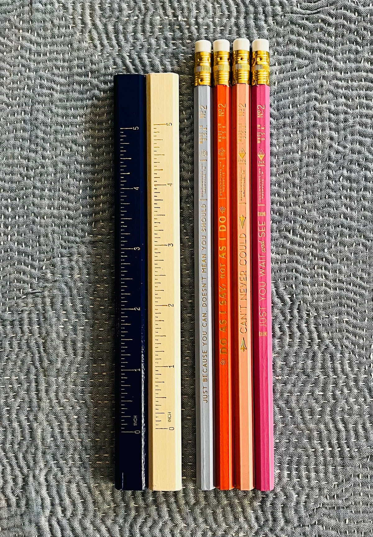 Six pencils with motivational phrases in orange and pink tones, shown with two rulers for scale