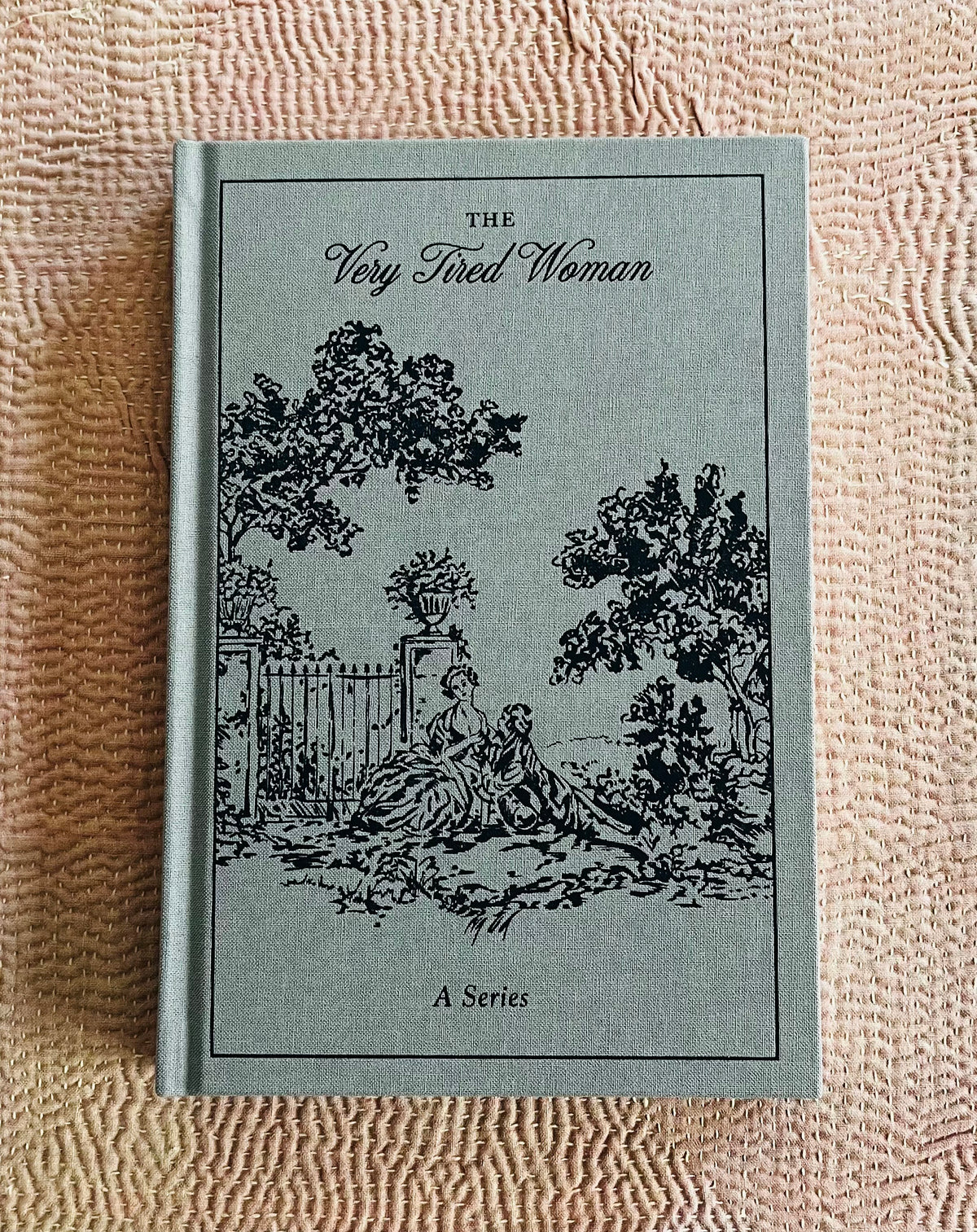 Gray cloth-bound journal titled The Very Tired Woman with black illustration of woman resting outdoors
