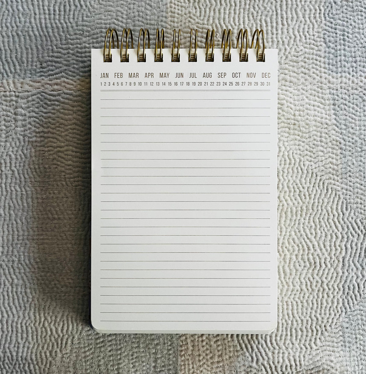 Spiral-bound notepad with months and dates at top, lined pages below