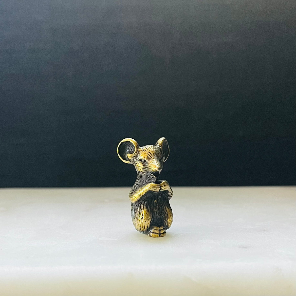 Small bronze mouse figurine standing upright holding paws together, front view