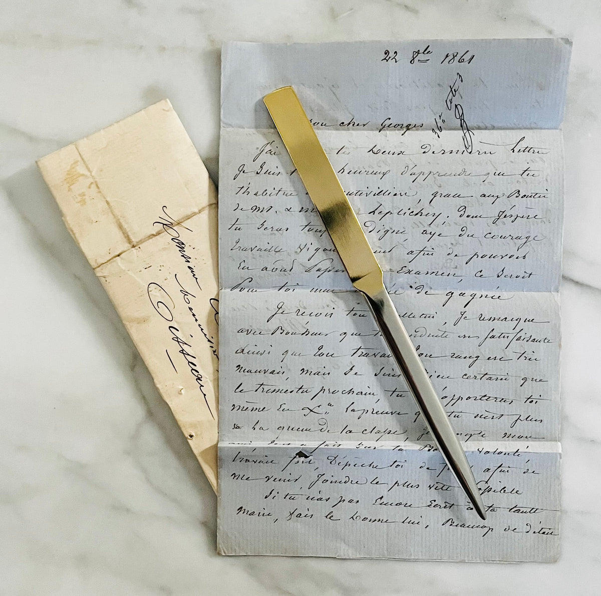 Brass letter opener with white handle resting on vintage handwritten letters from 1861