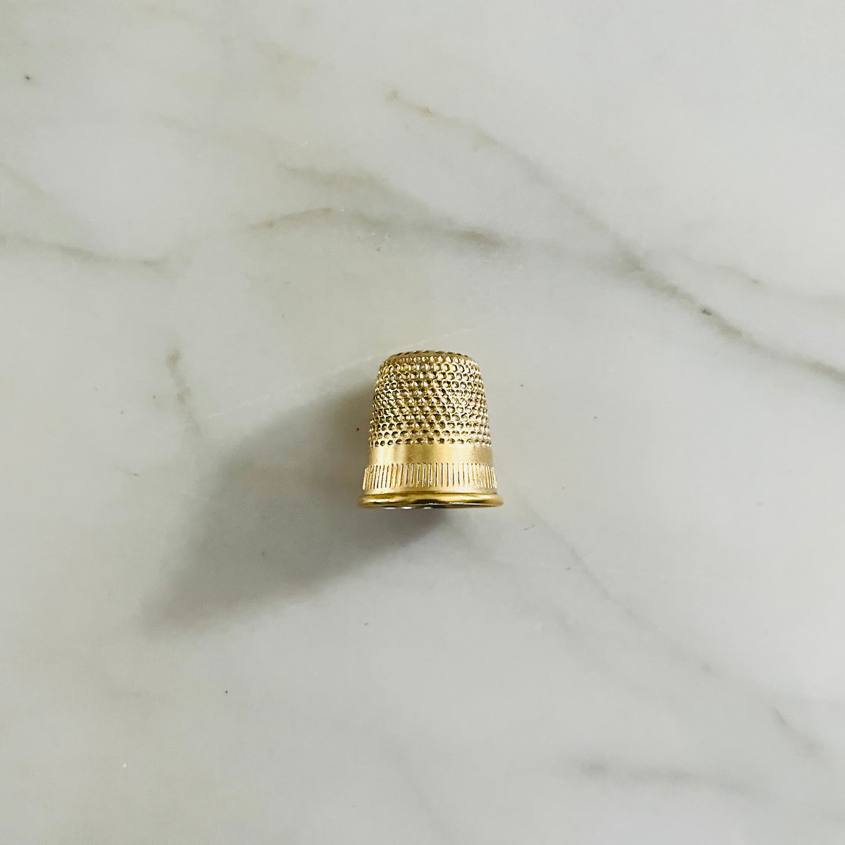 Gold thimble with dimpled top and ridged band on white marble surface