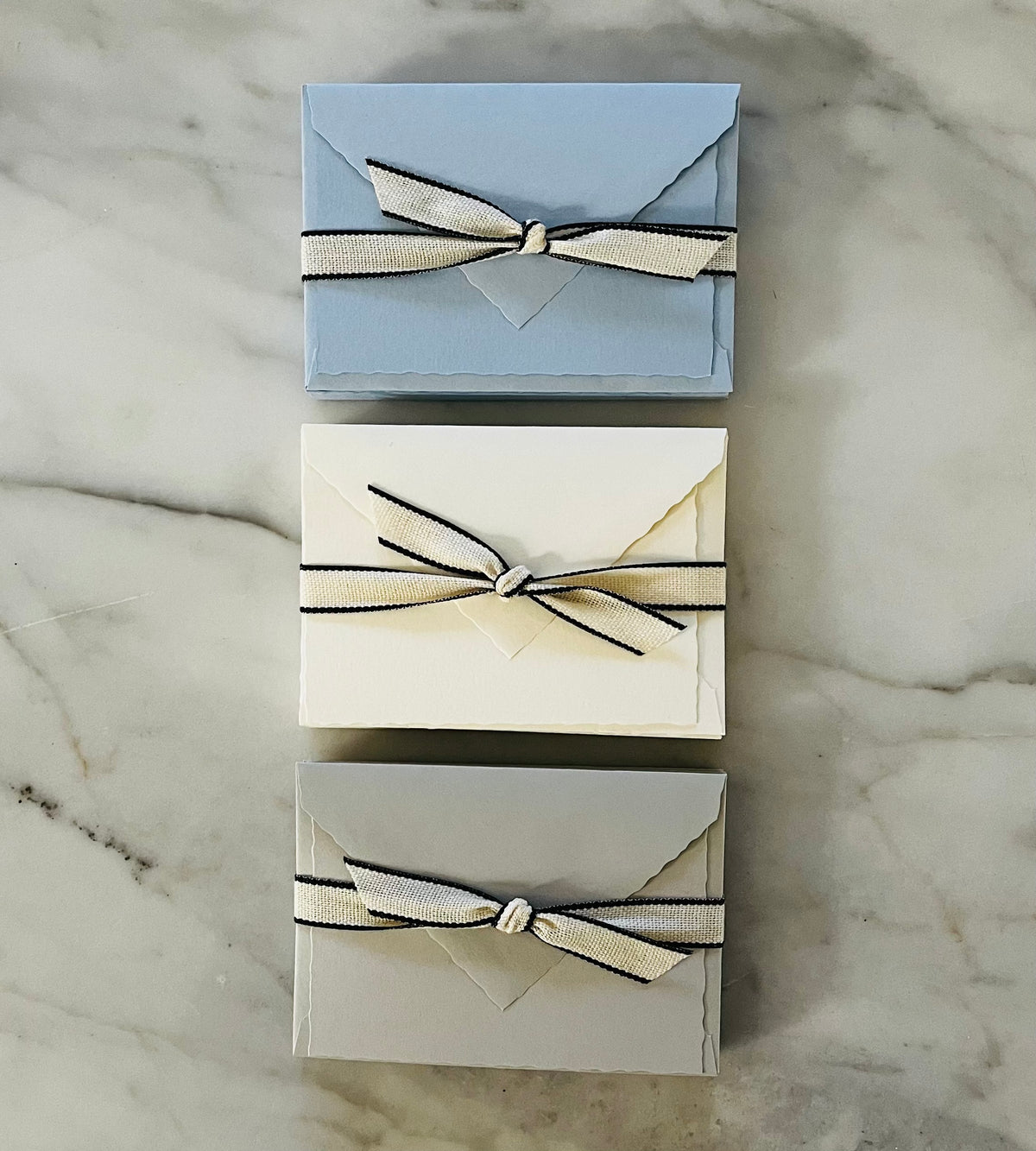 Three boxes of Italian note cards tied with cream and black striped ribbon on marble surface
