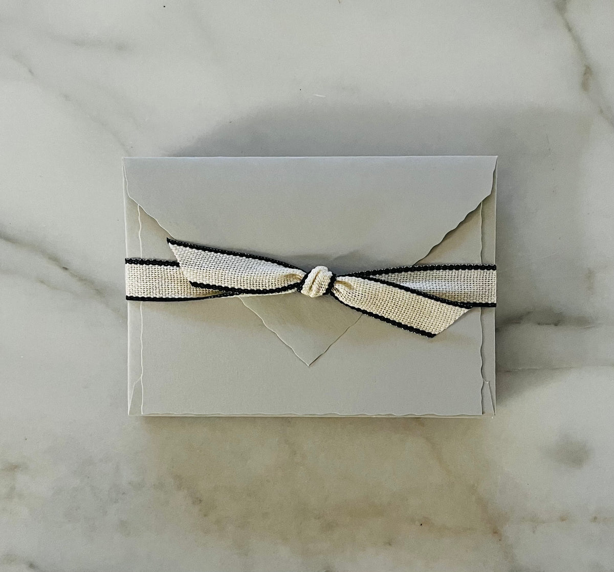 White Italian note card with deckled edges wrapped in beige and black ribbon bow