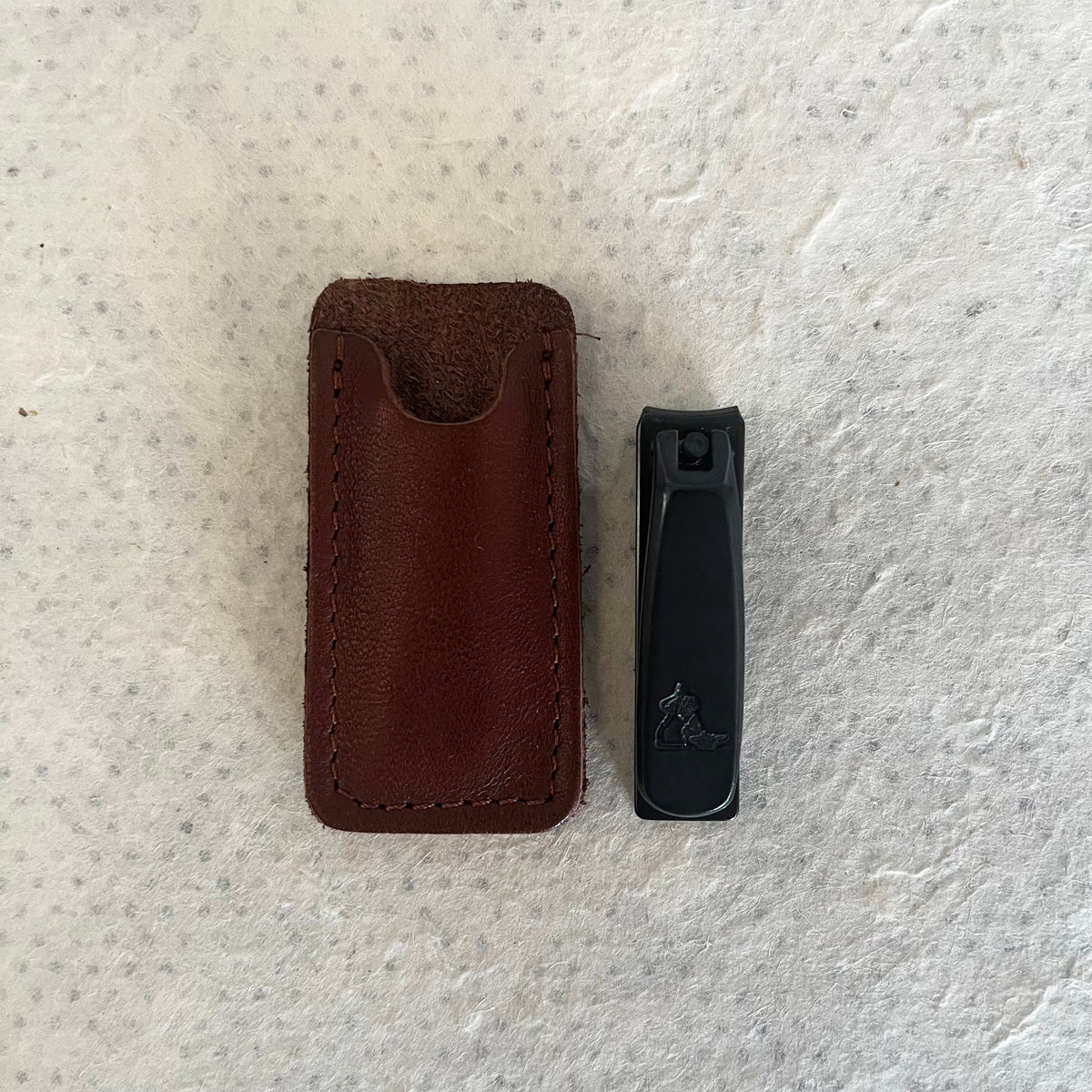 Black Italian nail clippers next to brown leather protective case on white fabric