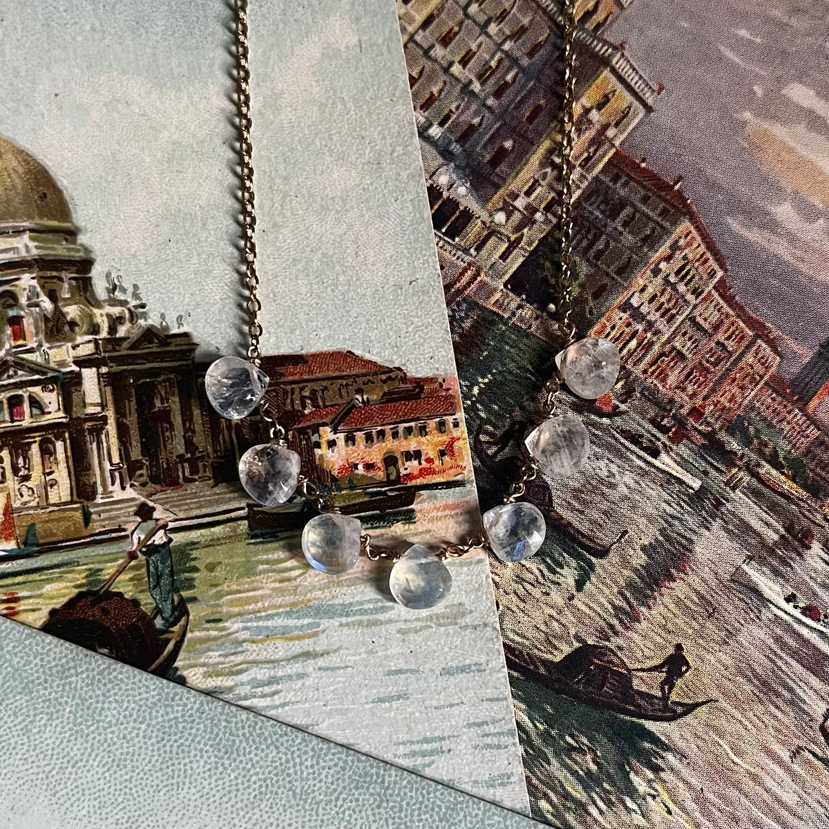 Dewdrop necklace with clear glass beads draped over vintage European cityscape postcards