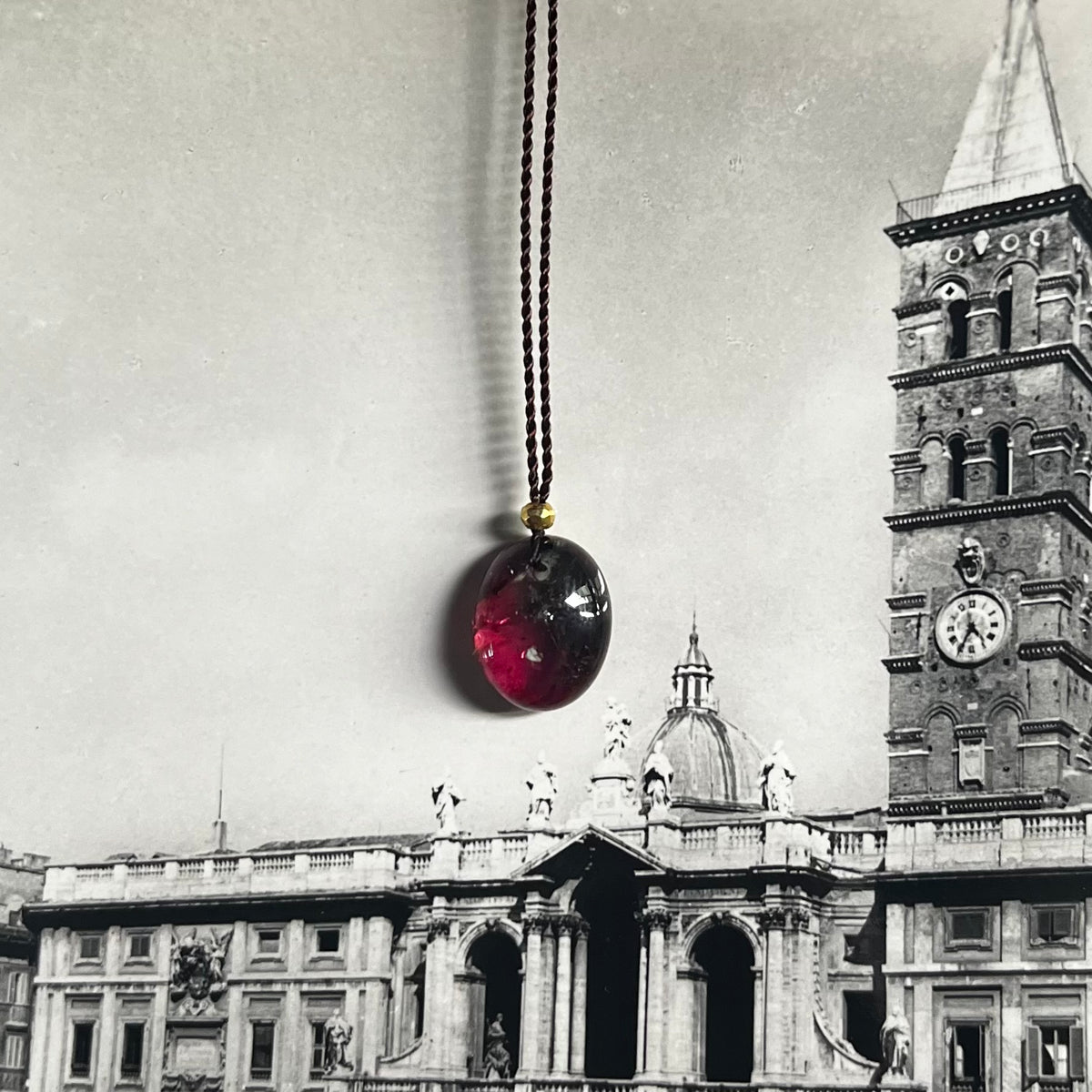 Tutti Frutti necklace with red and black spherical pendant on black cord, Italian architecture background