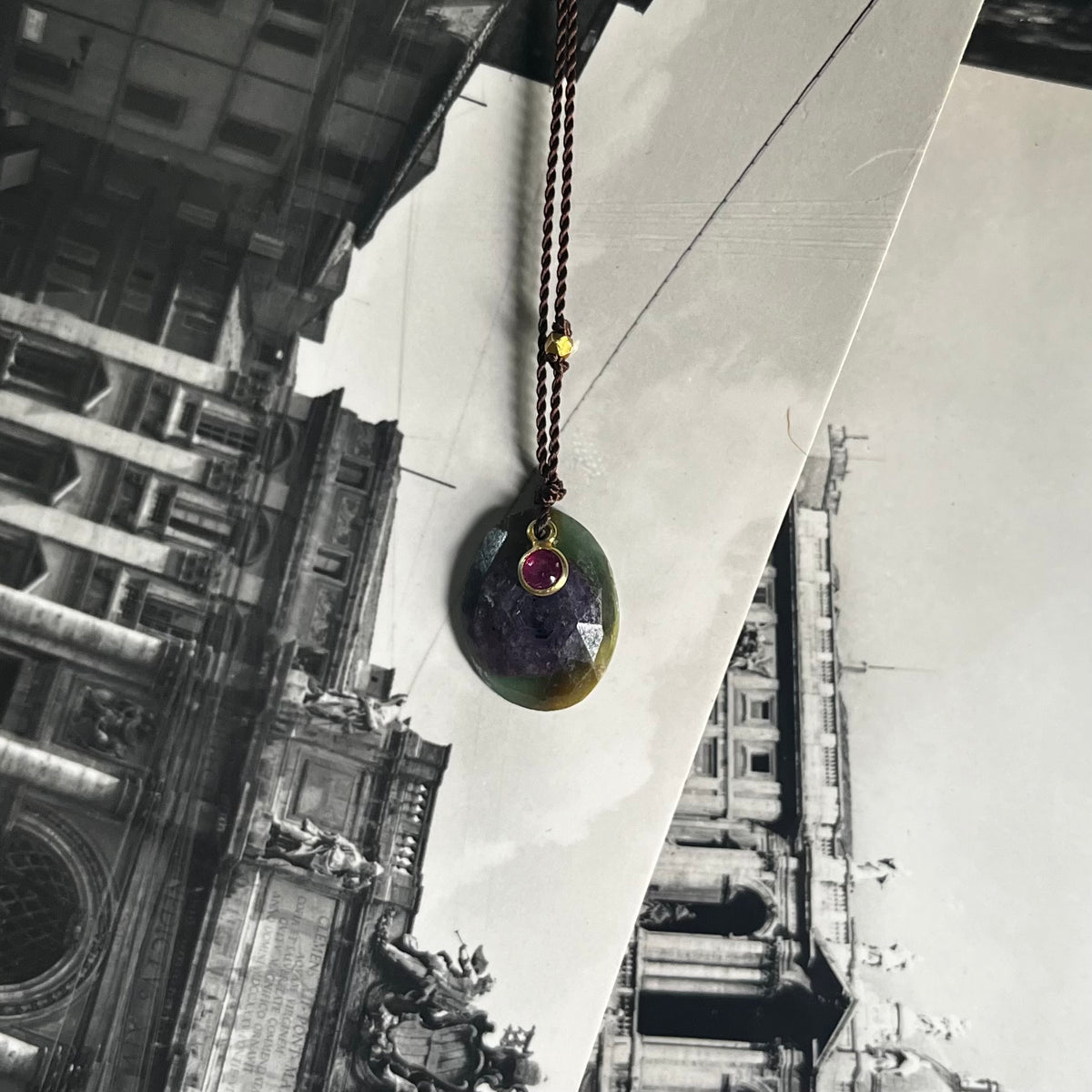 Match Made in Heaven Necklace with teardrop pendant and ruby stone, hanging outdoors against historic building