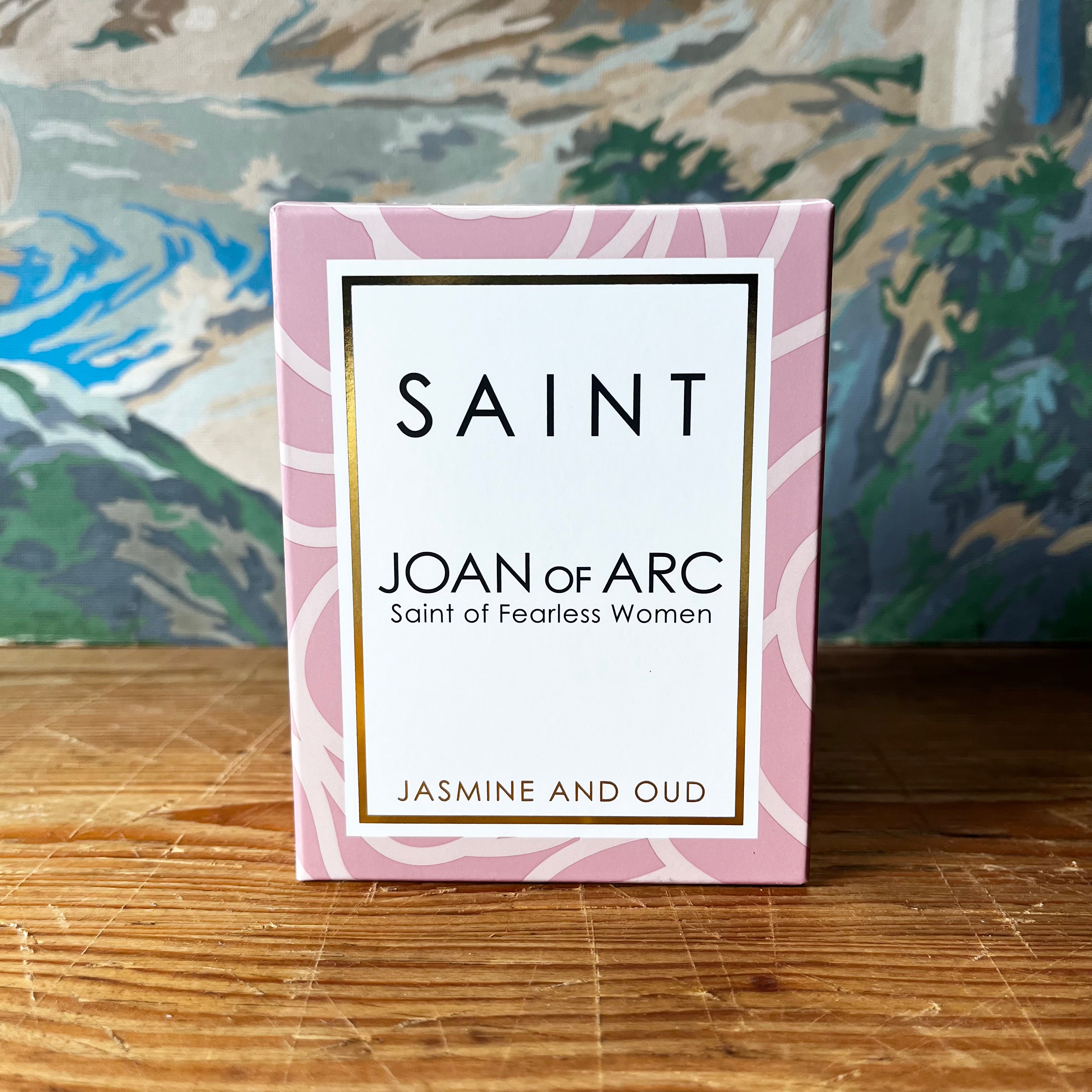 Pink Saint Joan of Arc candle box with jasmine and oud scent on wooden surface