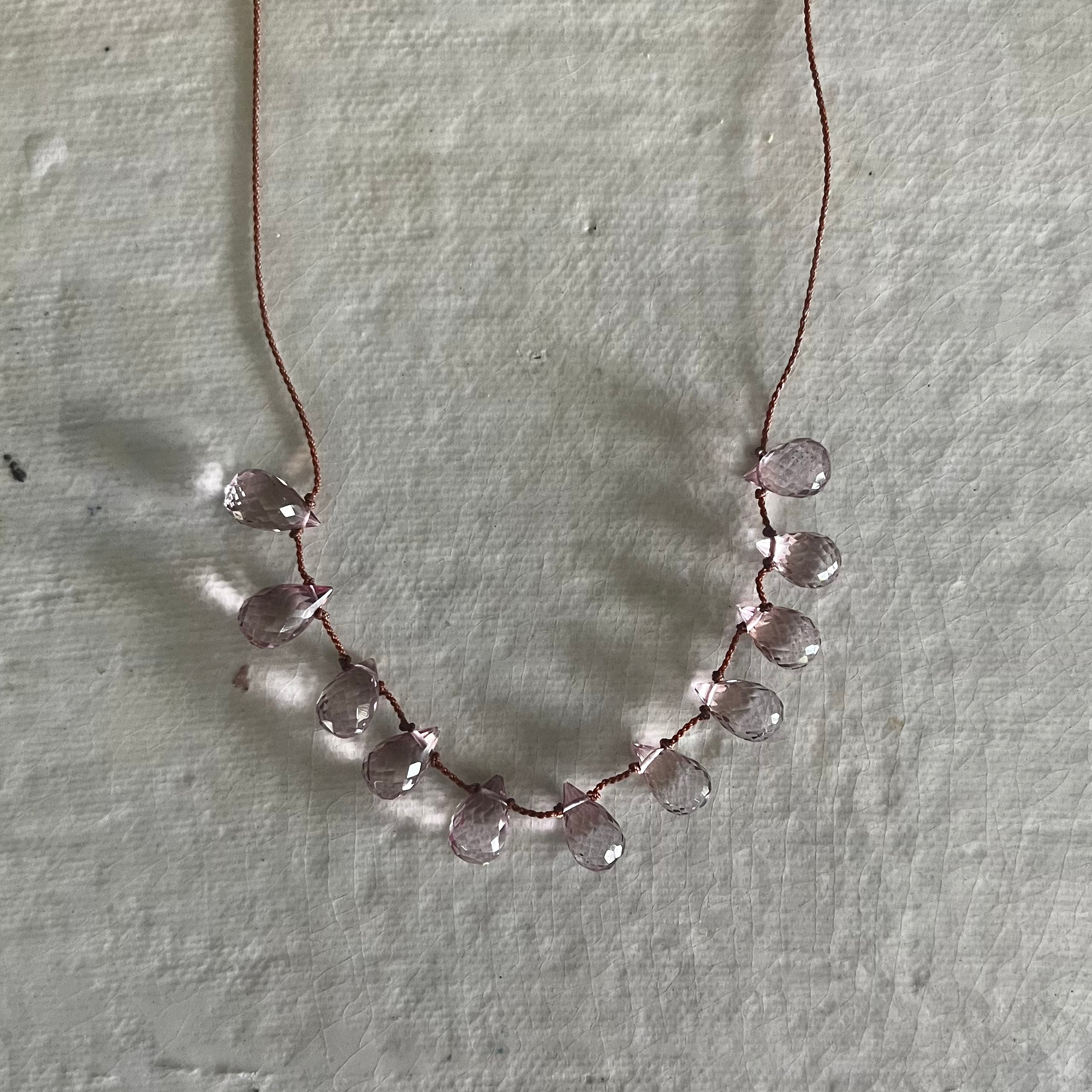 Rose quartz faceted briolette beads strung on brown cord necklace on white background