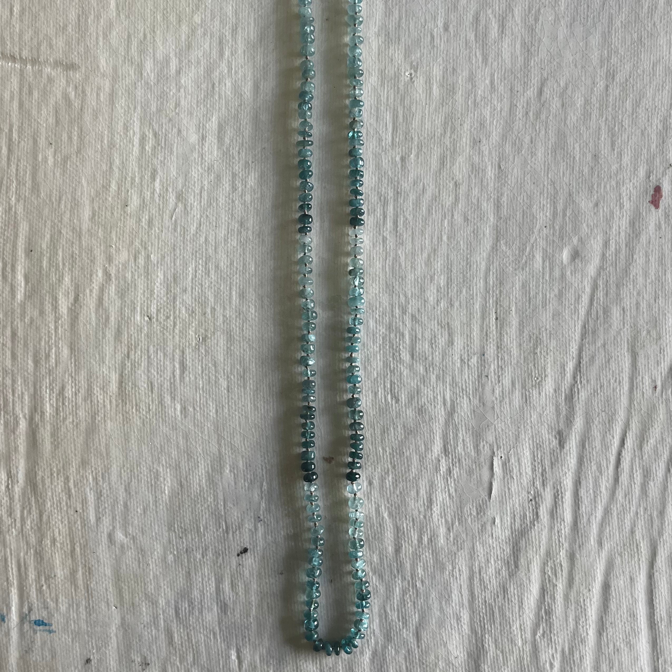 Grandidierite beaded necklace with blue-green gradient stones on light wood surface