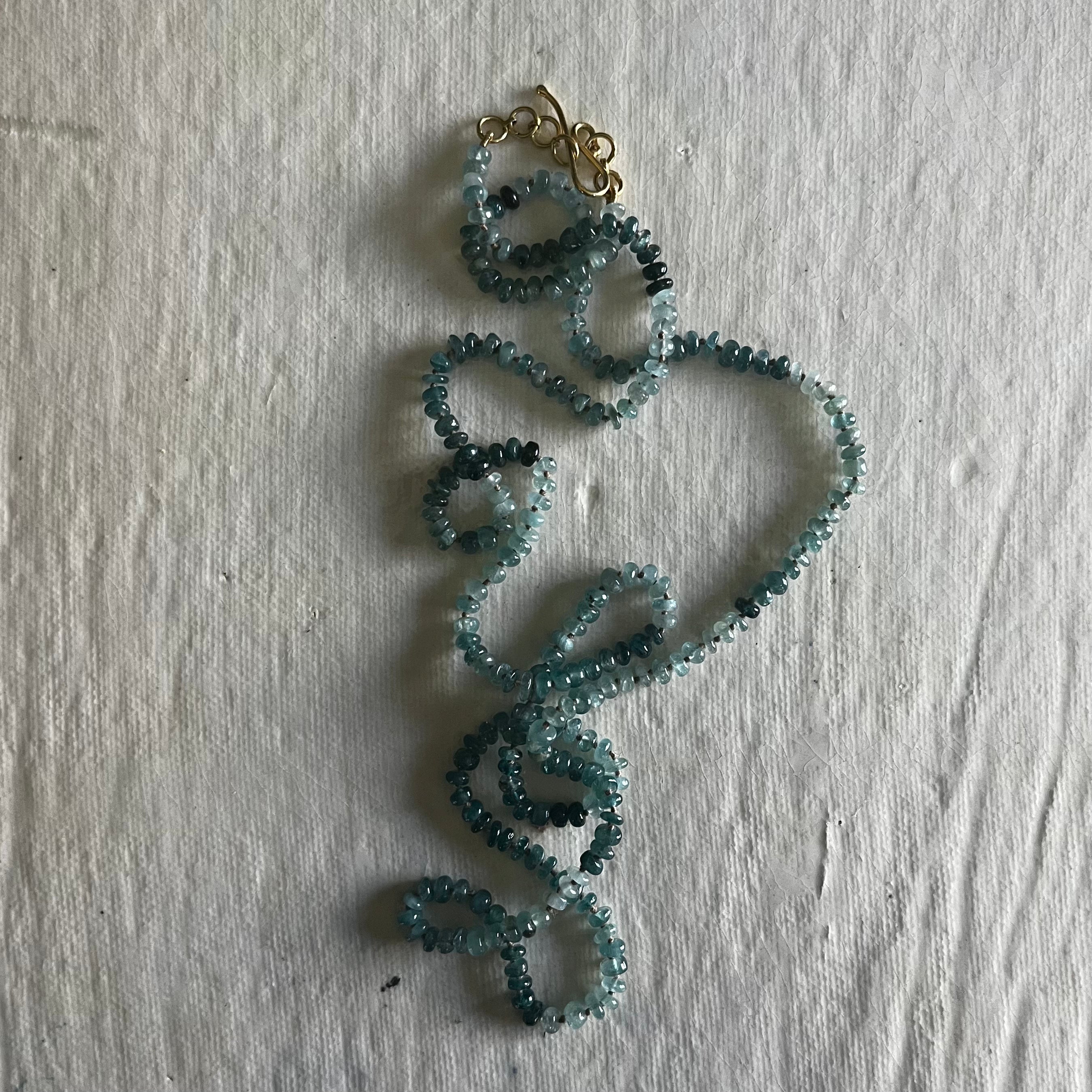 Grandidierite necklace with teal chip beads arranged in looping curves with gold clasp