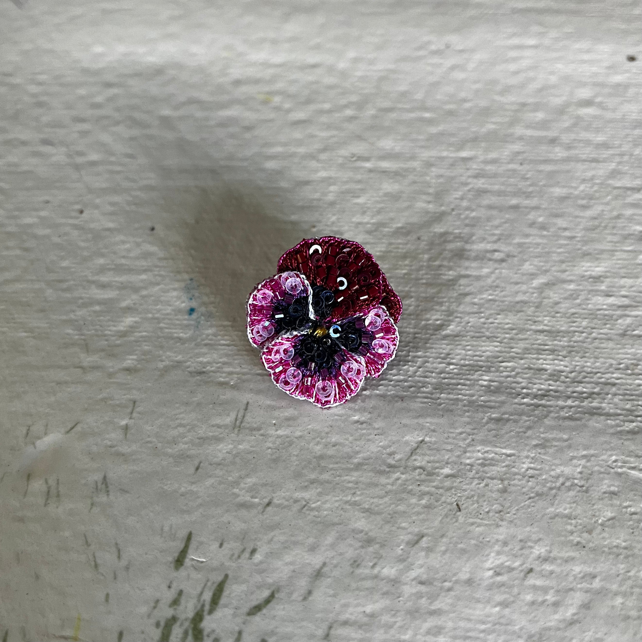 Rose Pansy Button Brooch with burgundy, pink and black beaded petals on white wooden surface