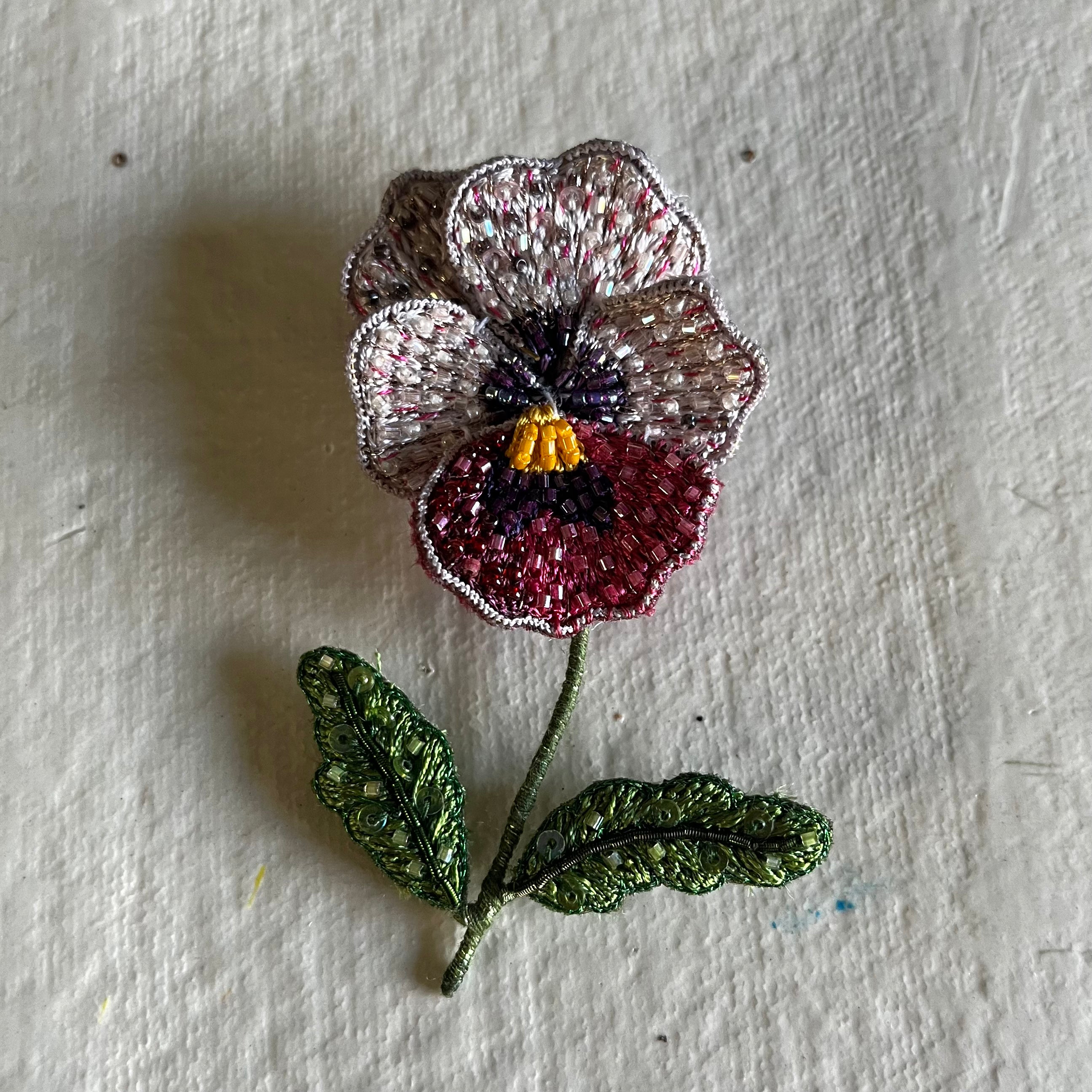 Pink Pansy Brooch with beaded petals, yellow center, and two green leaves on stem